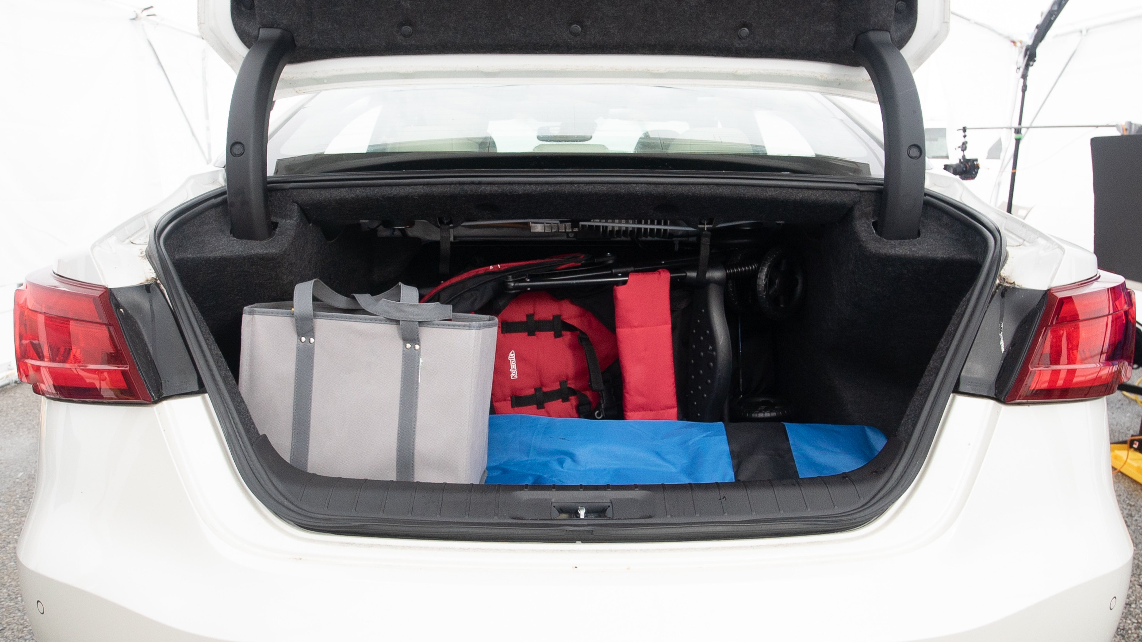 The trunk lid is open showing full view of the trunk. A baby stroller, three grocery carriers, one camping chairs in the carrying bag, and a set of golf clubs are placed inside.