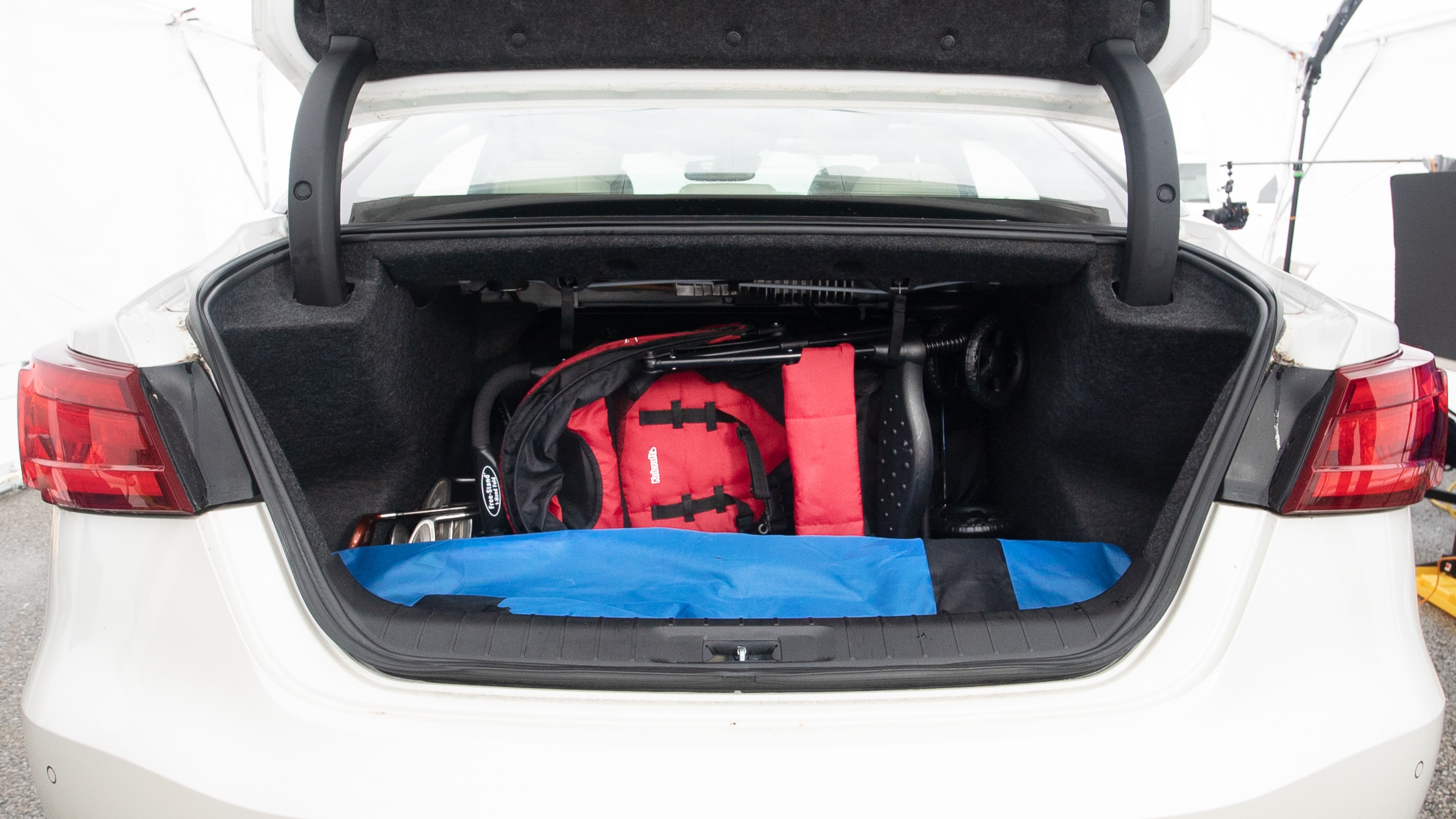 The trunk lid is open showing full view of the trunk. A baby stroller, three grocery carriers, one camping chairs in the carrying bag, and a set of golf clubs are placed inside.
