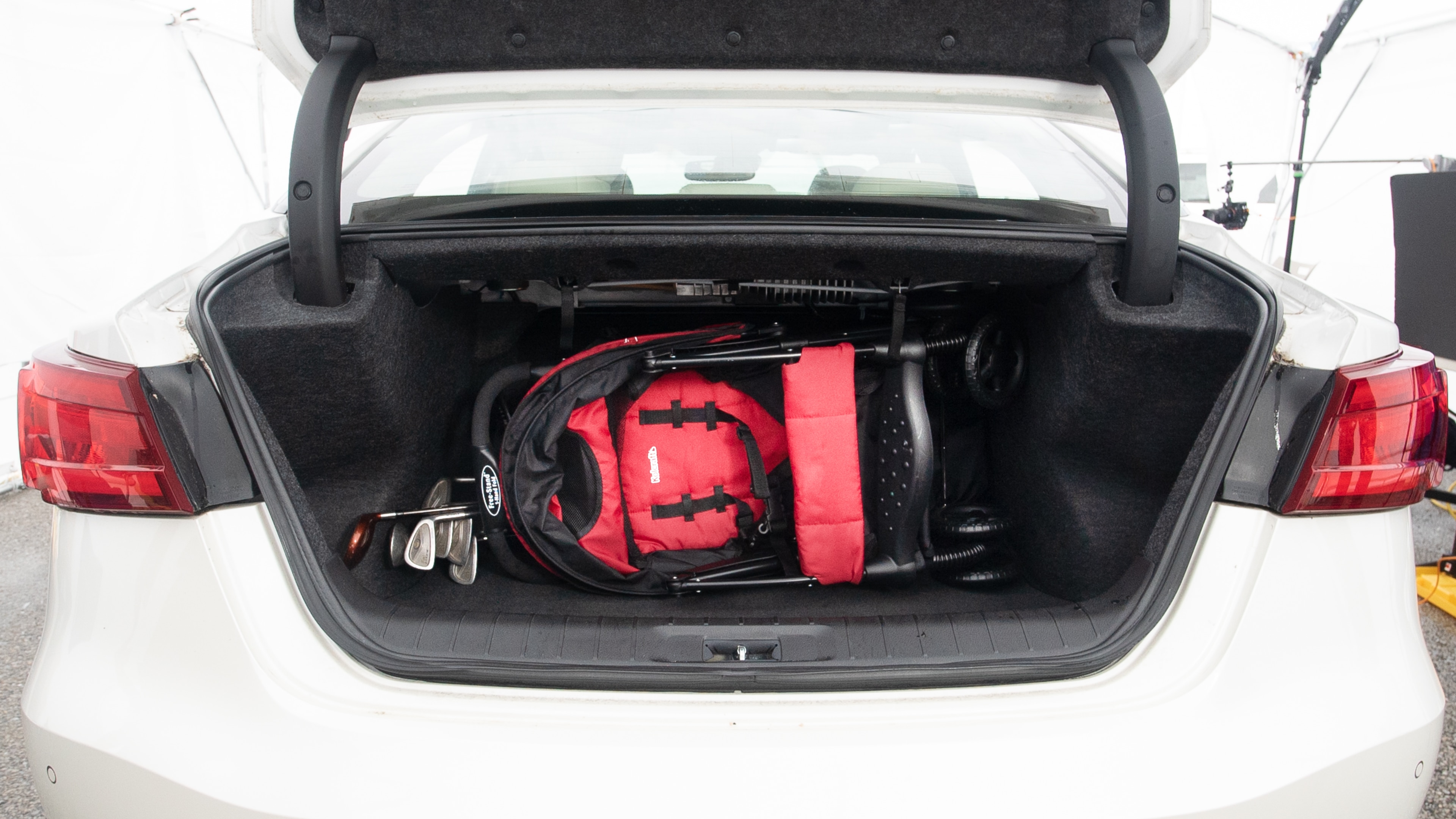 The trunk lid is open showing full view of the trunk. A baby stroller, three grocery carriers, one camping chairs in the carrying bag, and a set of golf clubs are placed inside.