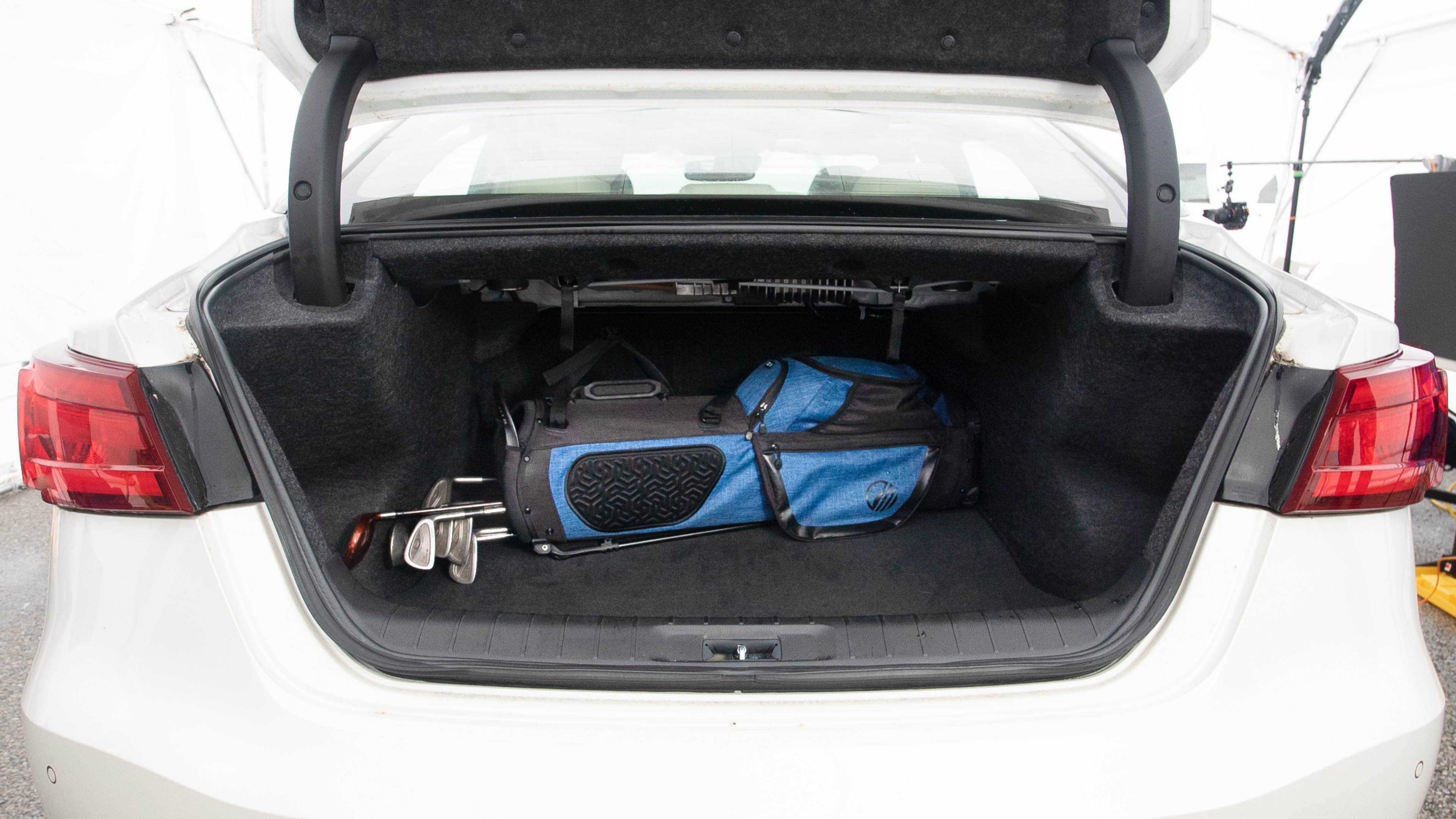 The trunk lid is open showing full view of the trunk. A baby stroller, three grocery carriers, one camping chairs in the carrying bag, and a set of golf clubs are placed inside.