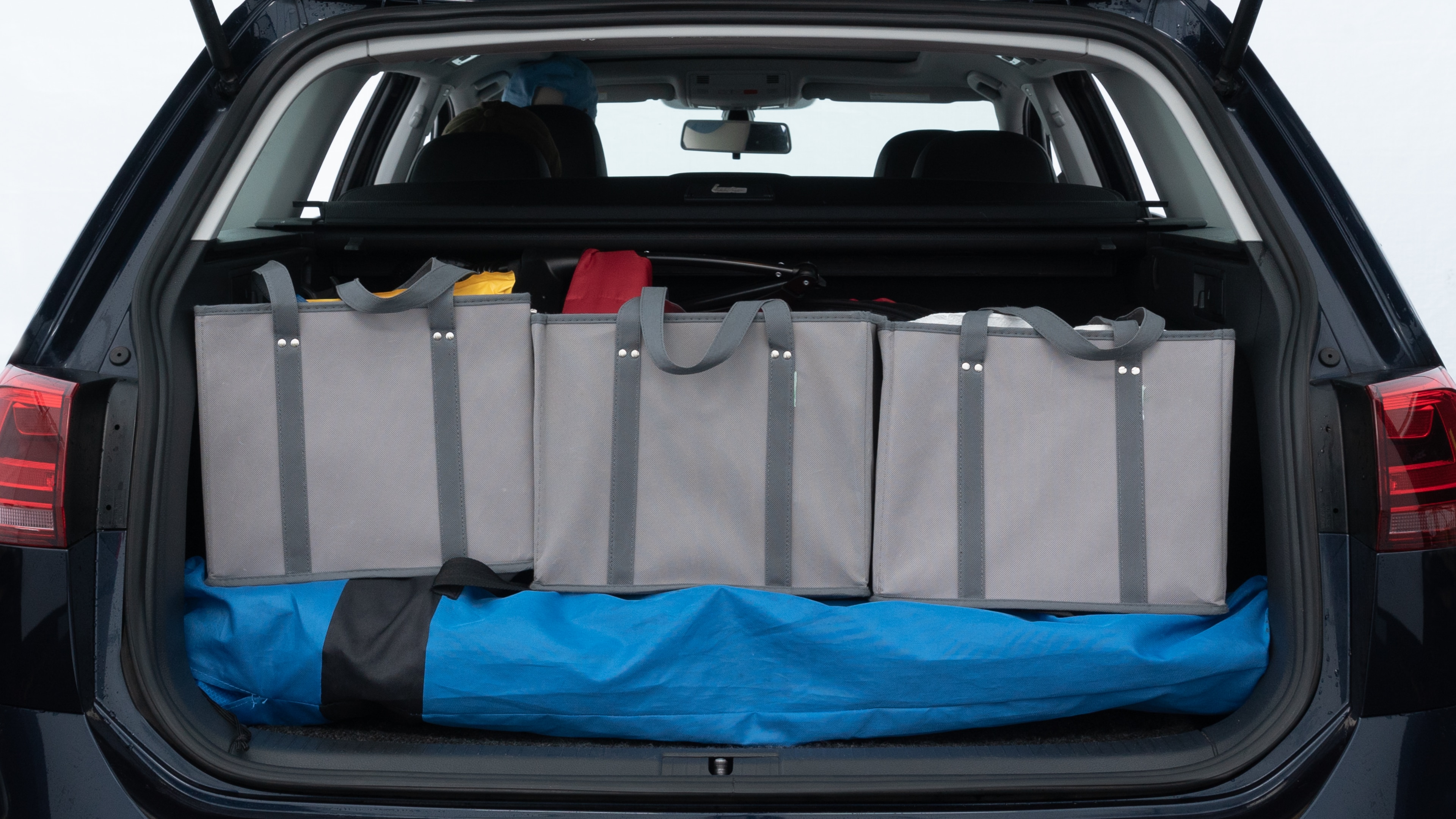 The trunk lid is open showing full view of the trunk. A baby stroller, three grocery carriers, two camping chairs in the carrying bag, and a set of golf clubs are placed inside.
