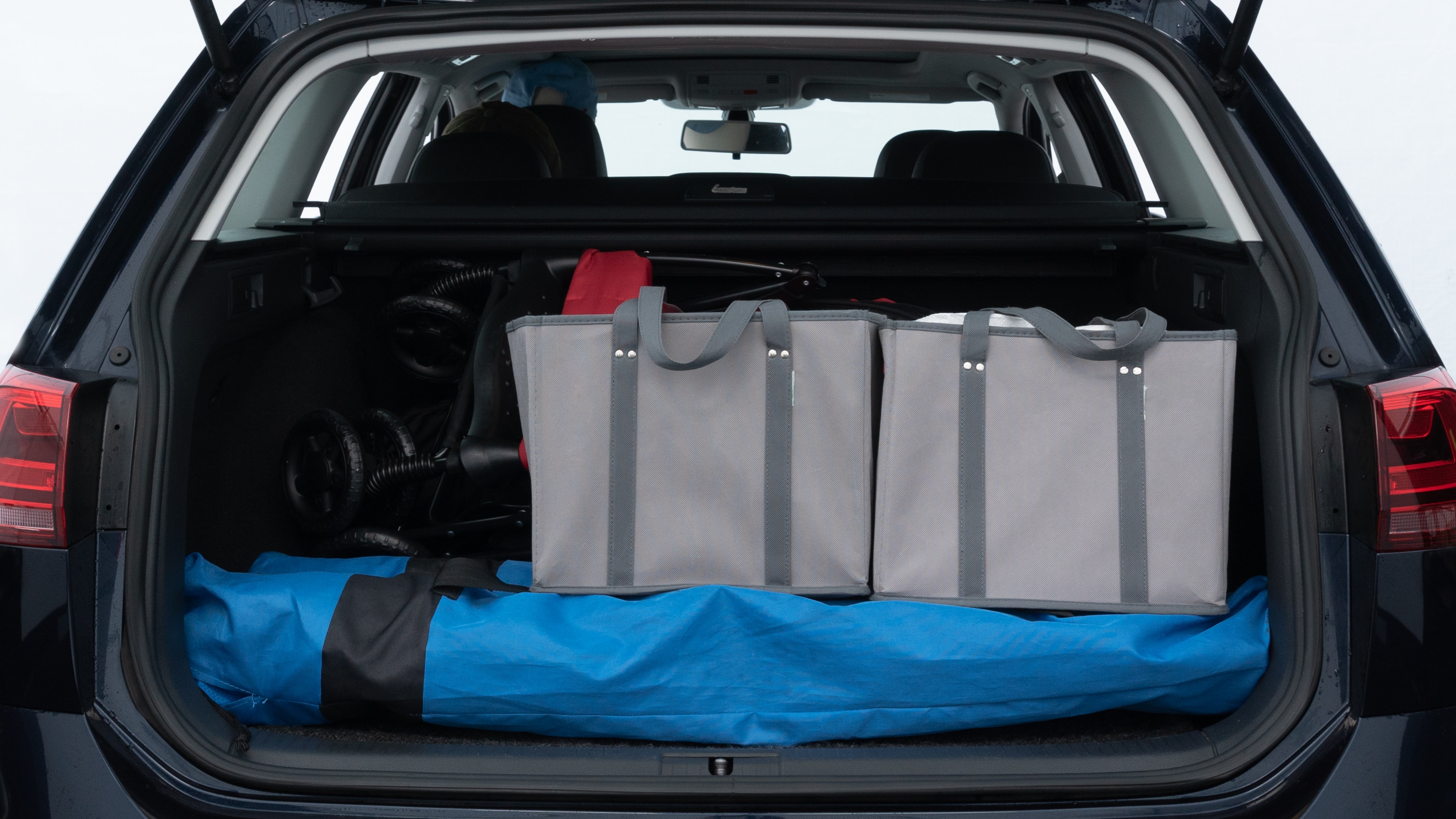 The trunk lid is open showing full view of the trunk. A baby stroller, three grocery carriers, two camping chairs in the carrying bag, and a set of golf clubs are placed inside.