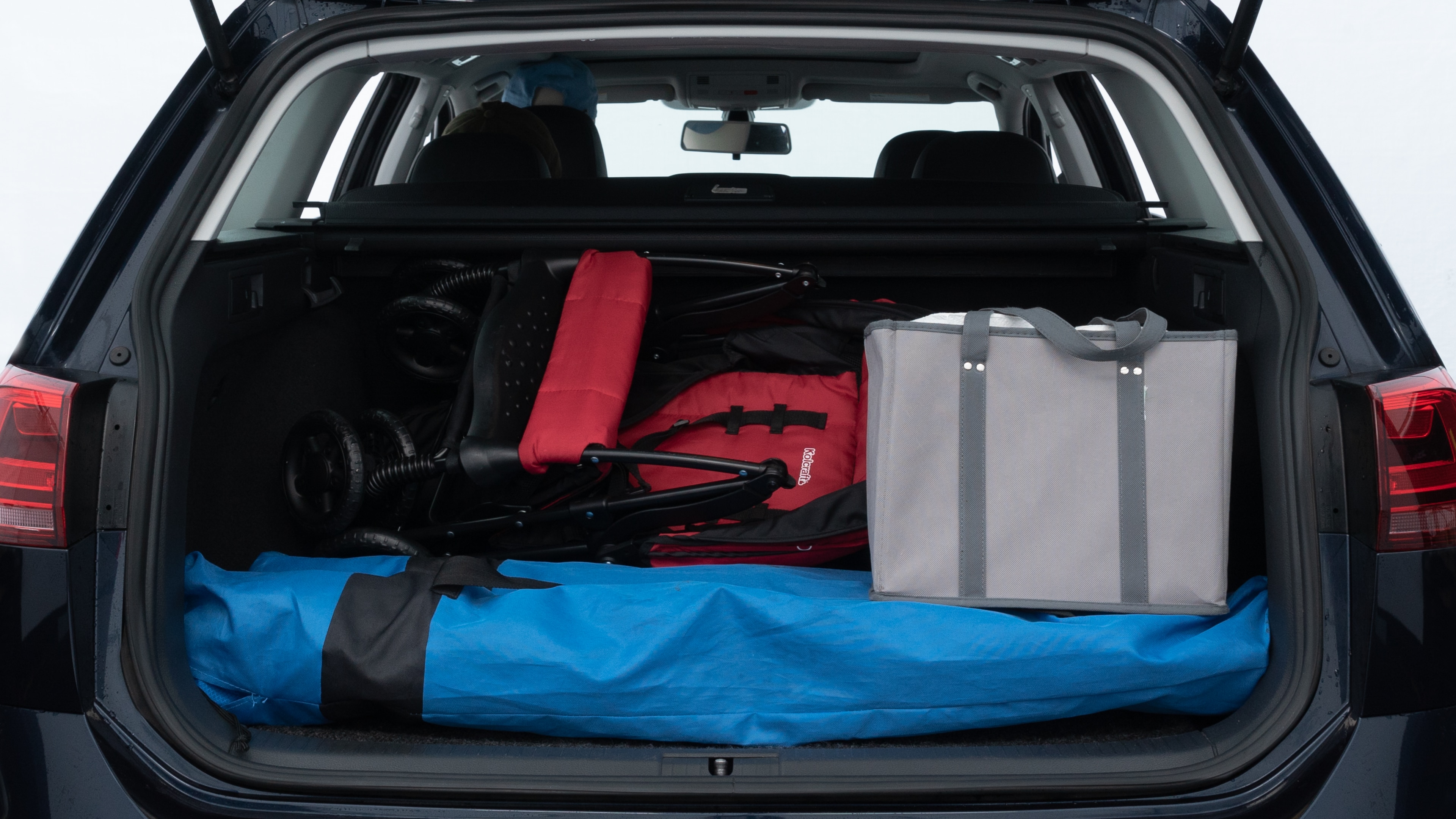 The trunk lid is open showing full view of the trunk. A baby stroller, three grocery carriers, two camping chairs in the carrying bag, and a set of golf clubs are placed inside.
