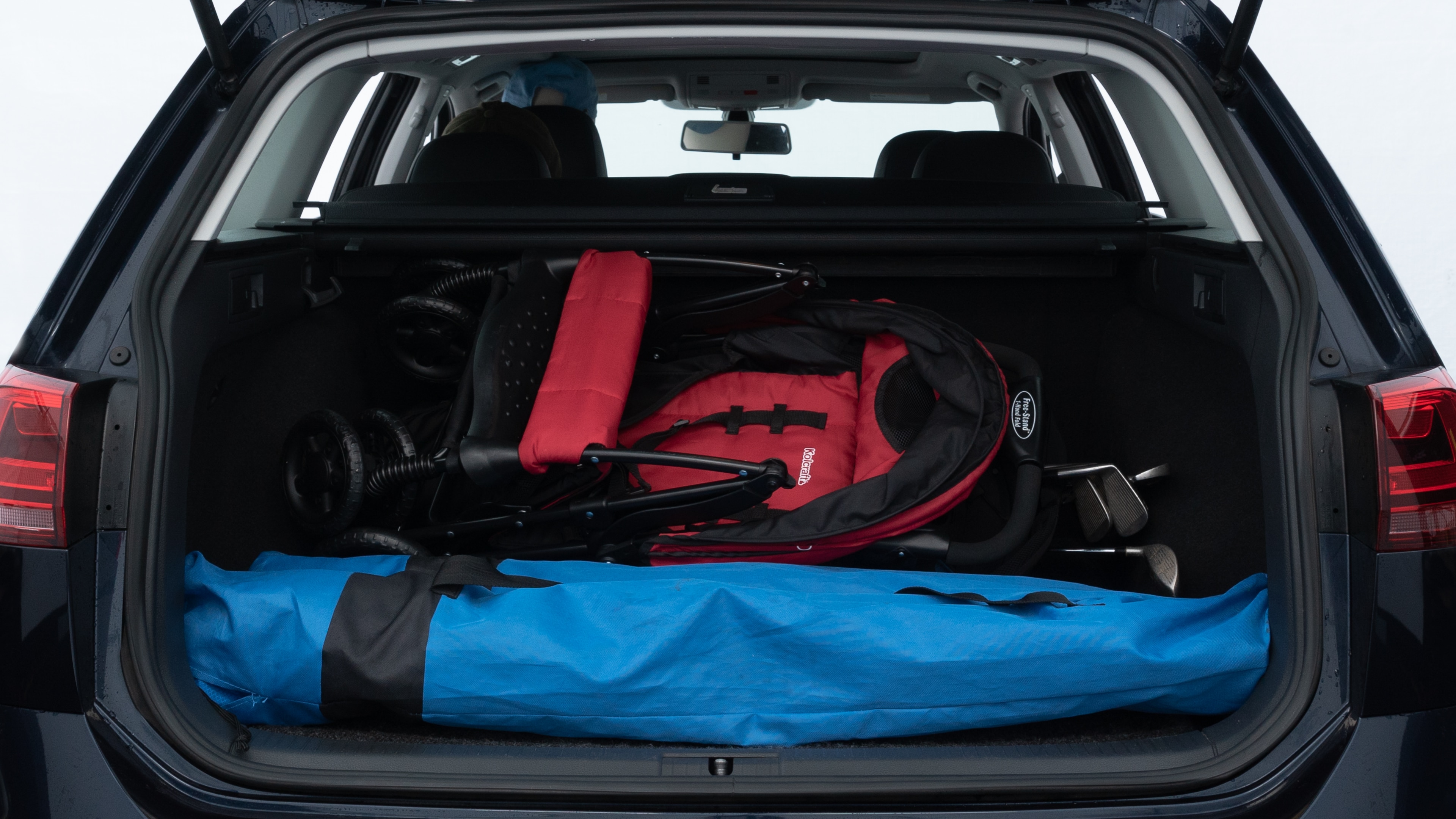 The trunk lid is open showing full view of the trunk. A baby stroller, three grocery carriers, two camping chairs in the carrying bag, and a set of golf clubs are placed inside.