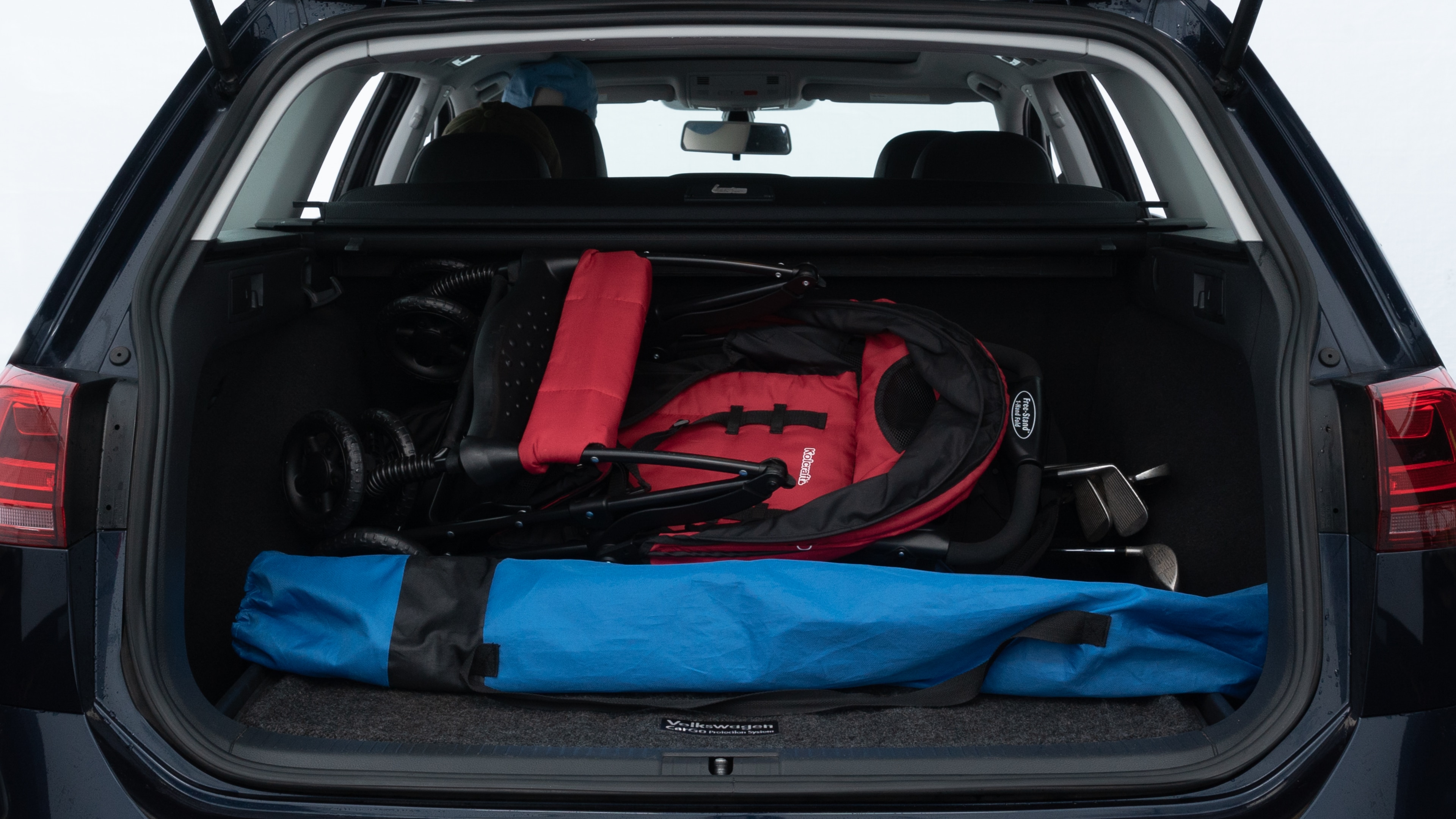 The trunk lid is open showing full view of the trunk. A baby stroller, three grocery carriers, two camping chairs in the carrying bag, and a set of golf clubs are placed inside.