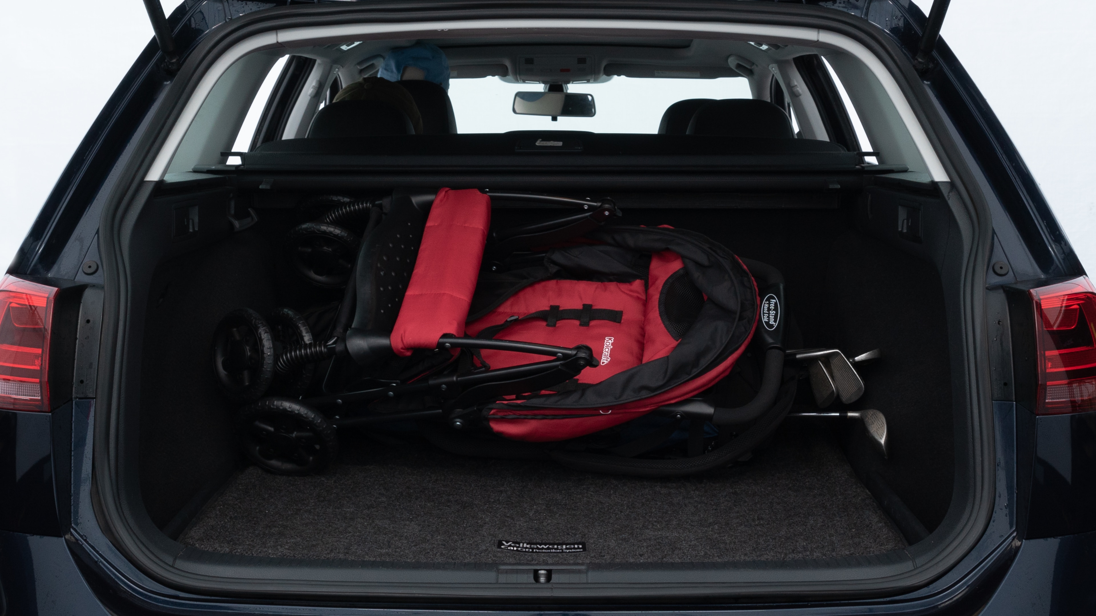 The trunk lid is open showing full view of the trunk. A baby stroller, three grocery carriers, two camping chairs in the carrying bag, and a set of golf clubs are placed inside.