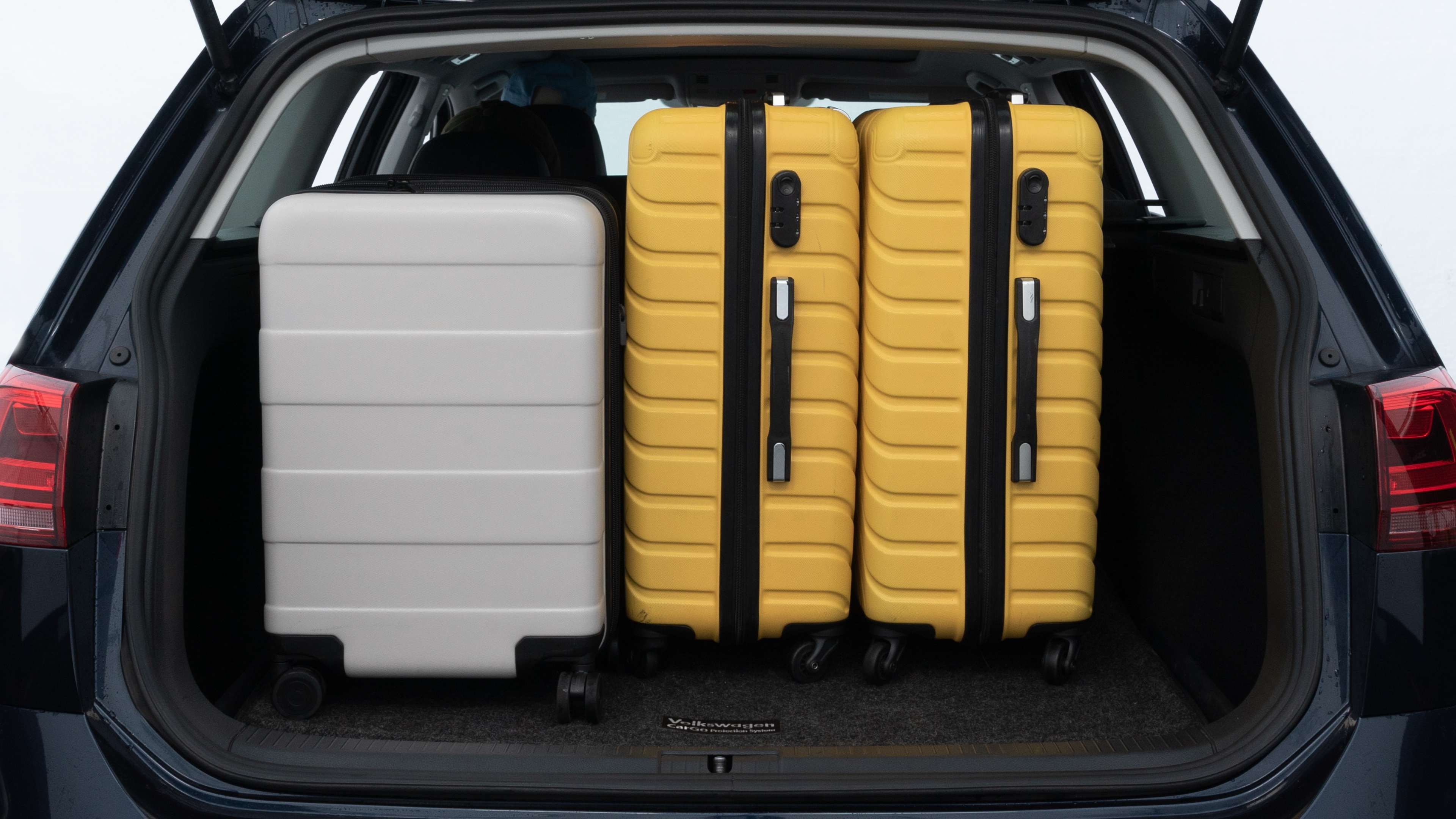The trunk lid is open, showing full view of the trunk space. Two medium and two small suitcases are placed inside.