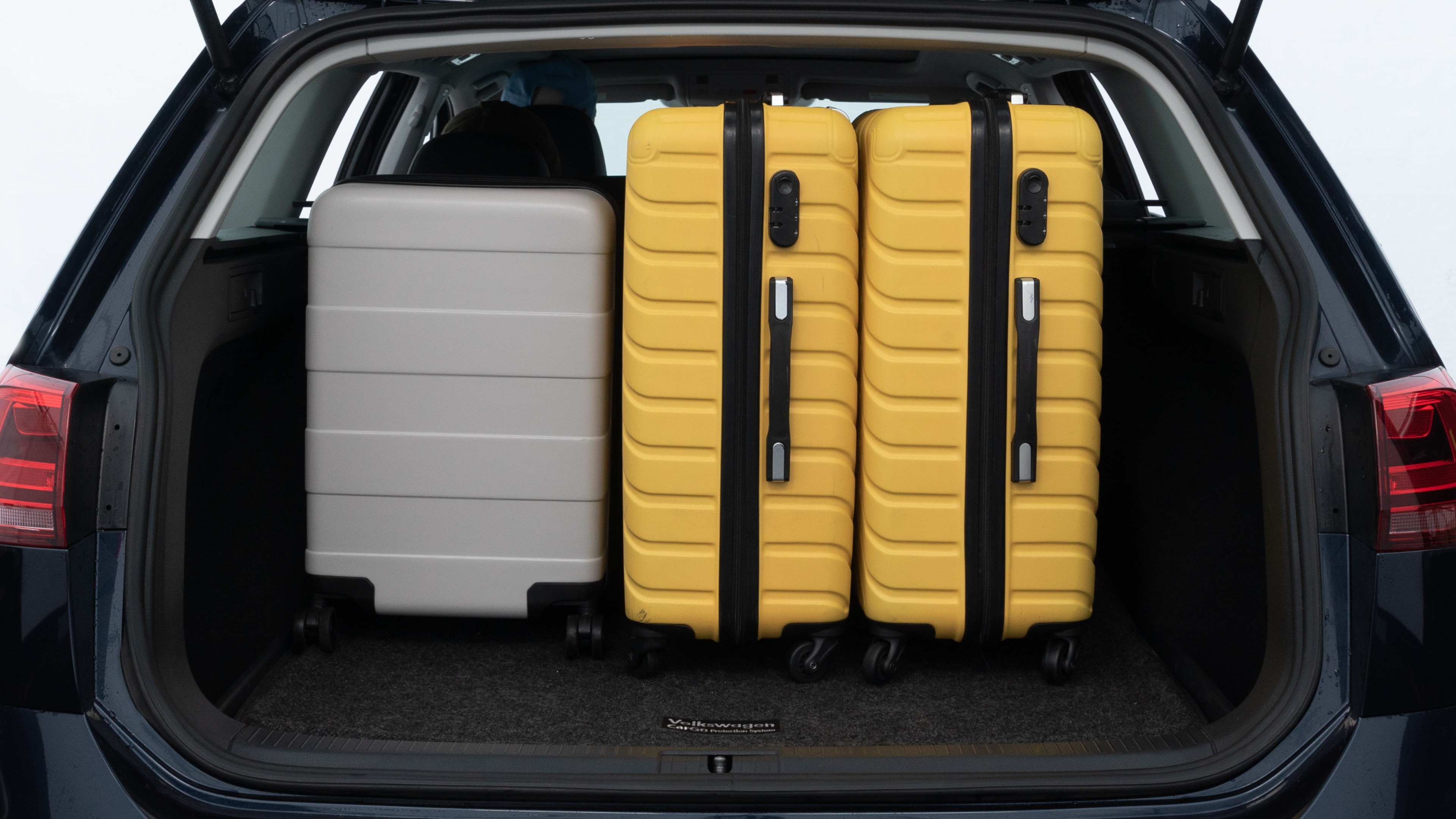The trunk lid is open, showing full view of the trunk space. Two medium and two small suitcases are placed inside.