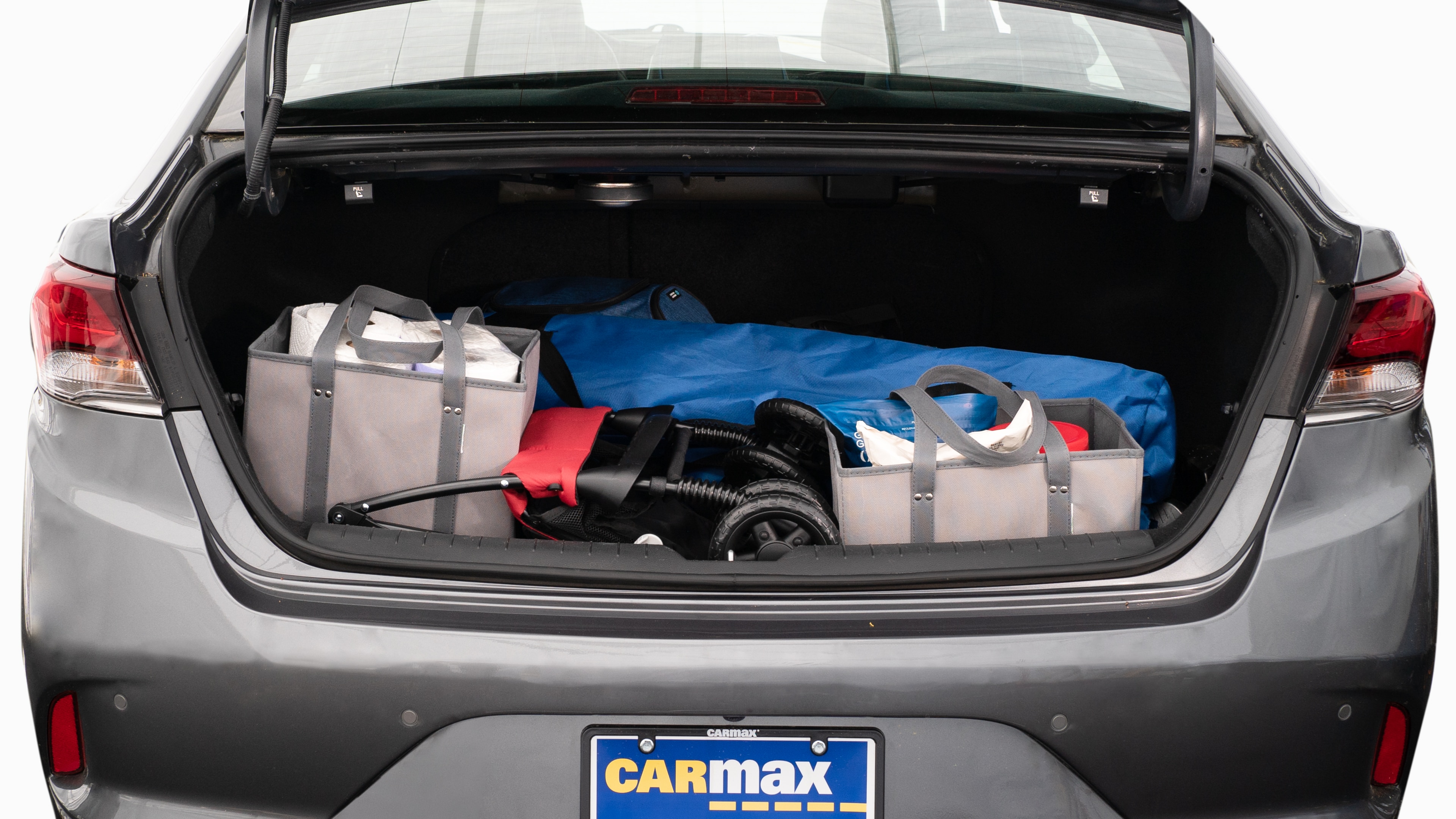 The trunk lid is open showing full view of the trunk. A baby stroller, two grocery carriers, two camping chairs in the carrying bag, and a set of golf clubs are placed inside.