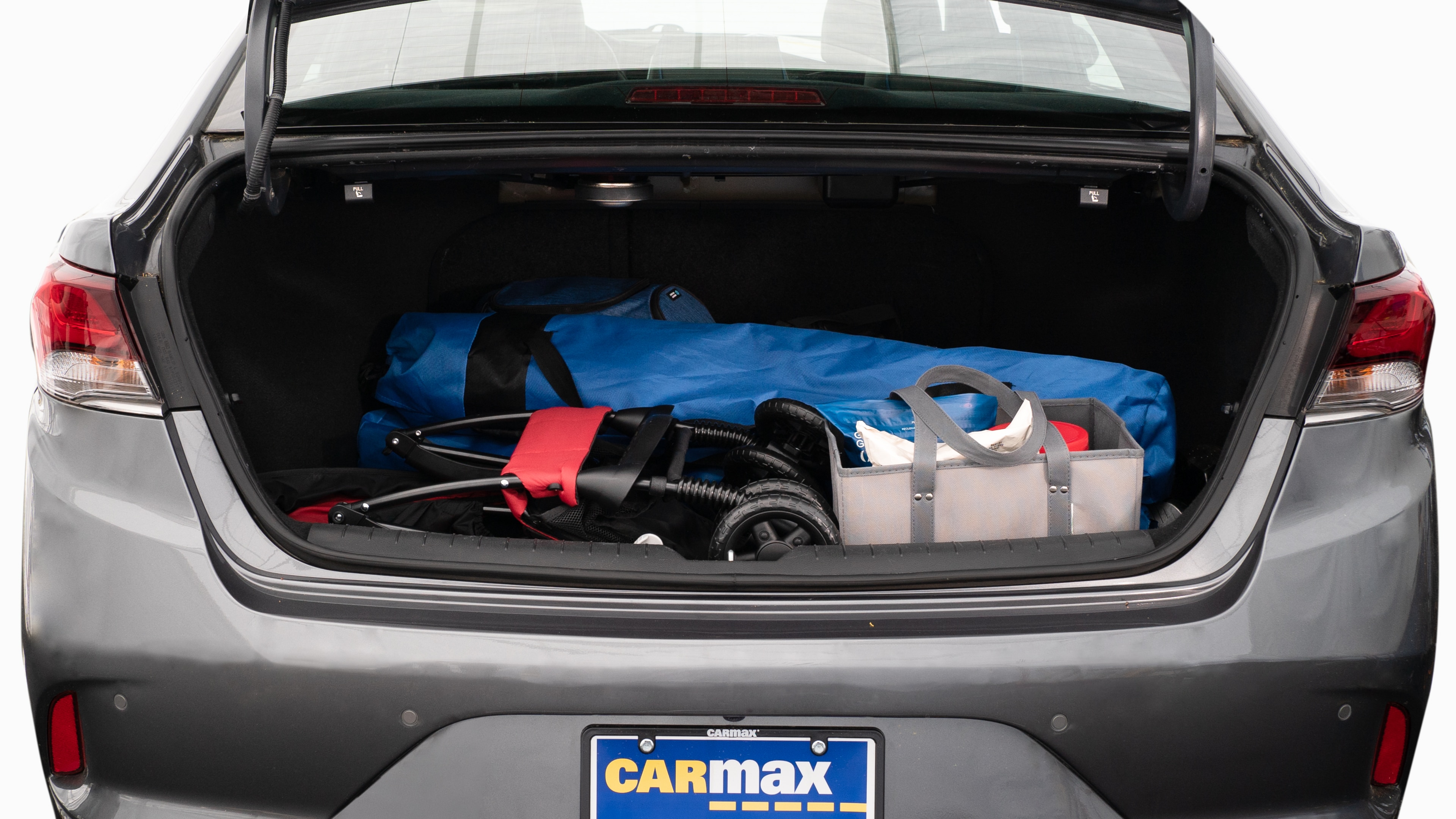 The trunk lid is open showing full view of the trunk. A baby stroller, two grocery carriers, two camping chairs in the carrying bag, and a set of golf clubs are placed inside.