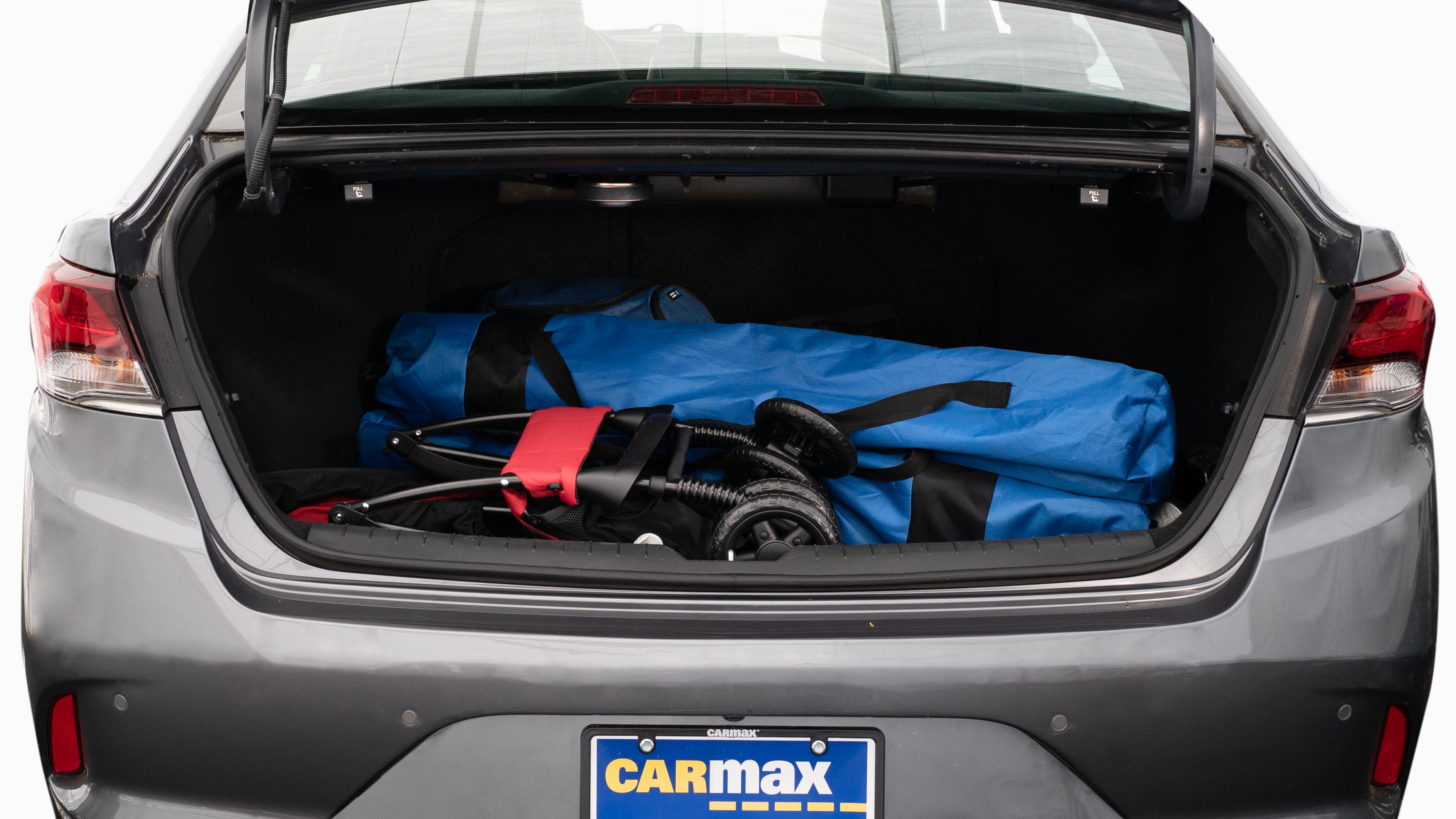 The trunk lid is open showing full view of the trunk. A baby stroller, two grocery carriers, two camping chairs in the carrying bag, and a set of golf clubs are placed inside.