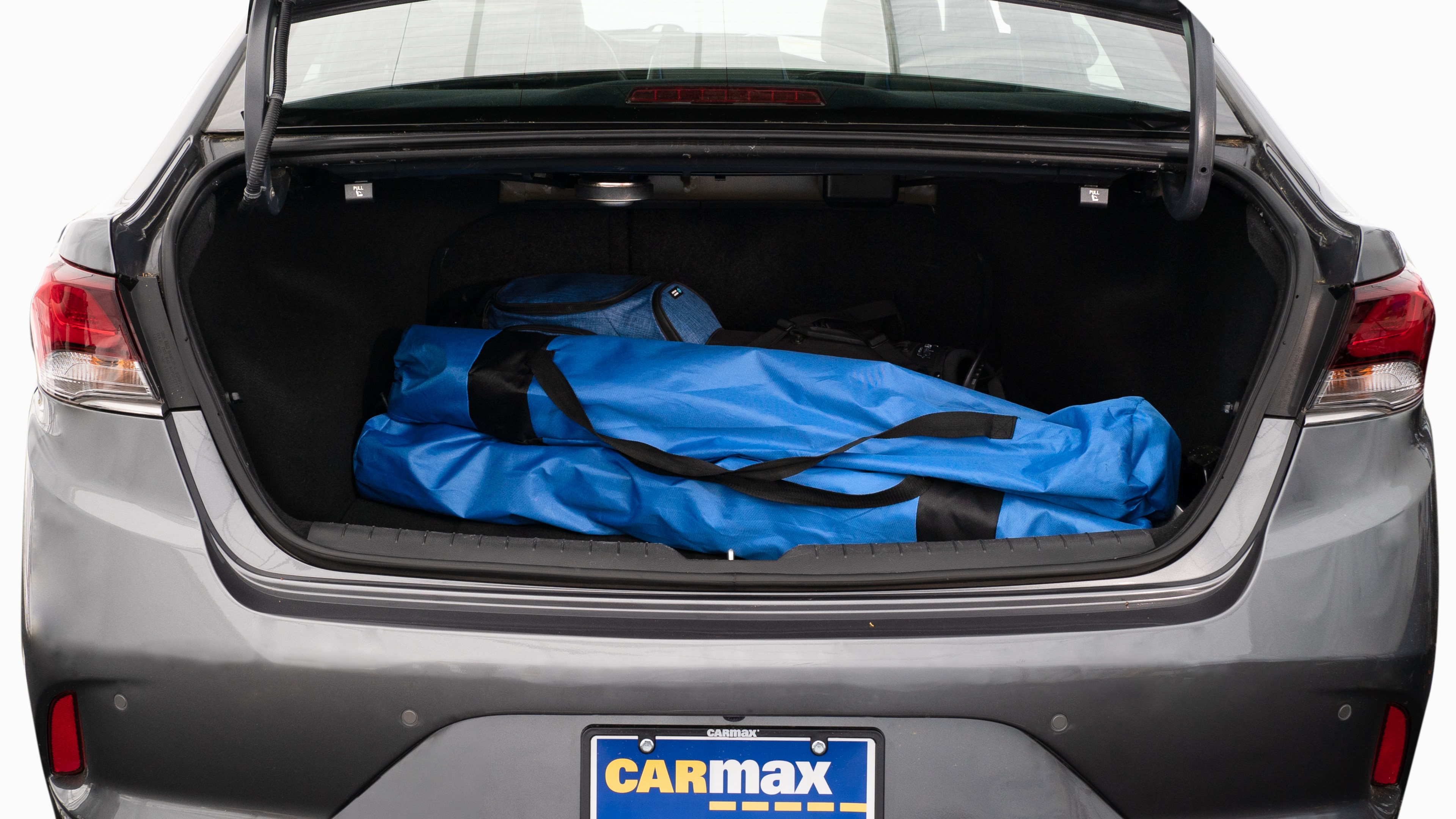 The trunk lid is open showing full view of the trunk. A baby stroller, two grocery carriers, two camping chairs in the carrying bag, and a set of golf clubs are placed inside.