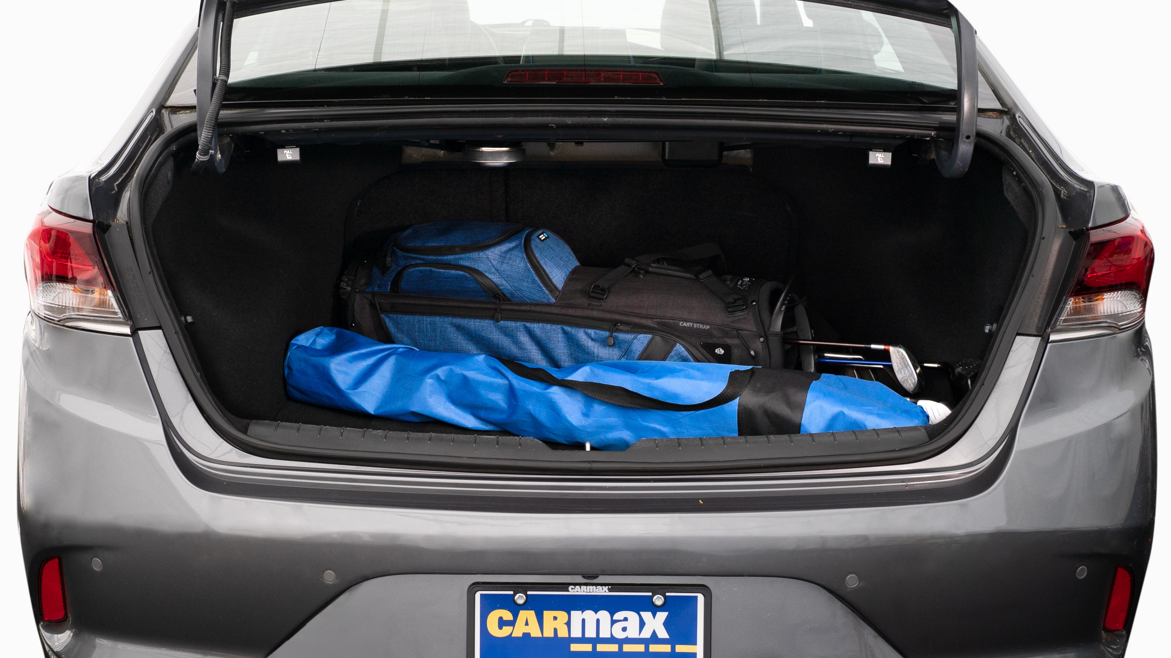 The trunk lid is open showing full view of the trunk. A baby stroller, two grocery carriers, two camping chairs in the carrying bag, and a set of golf clubs are placed inside.