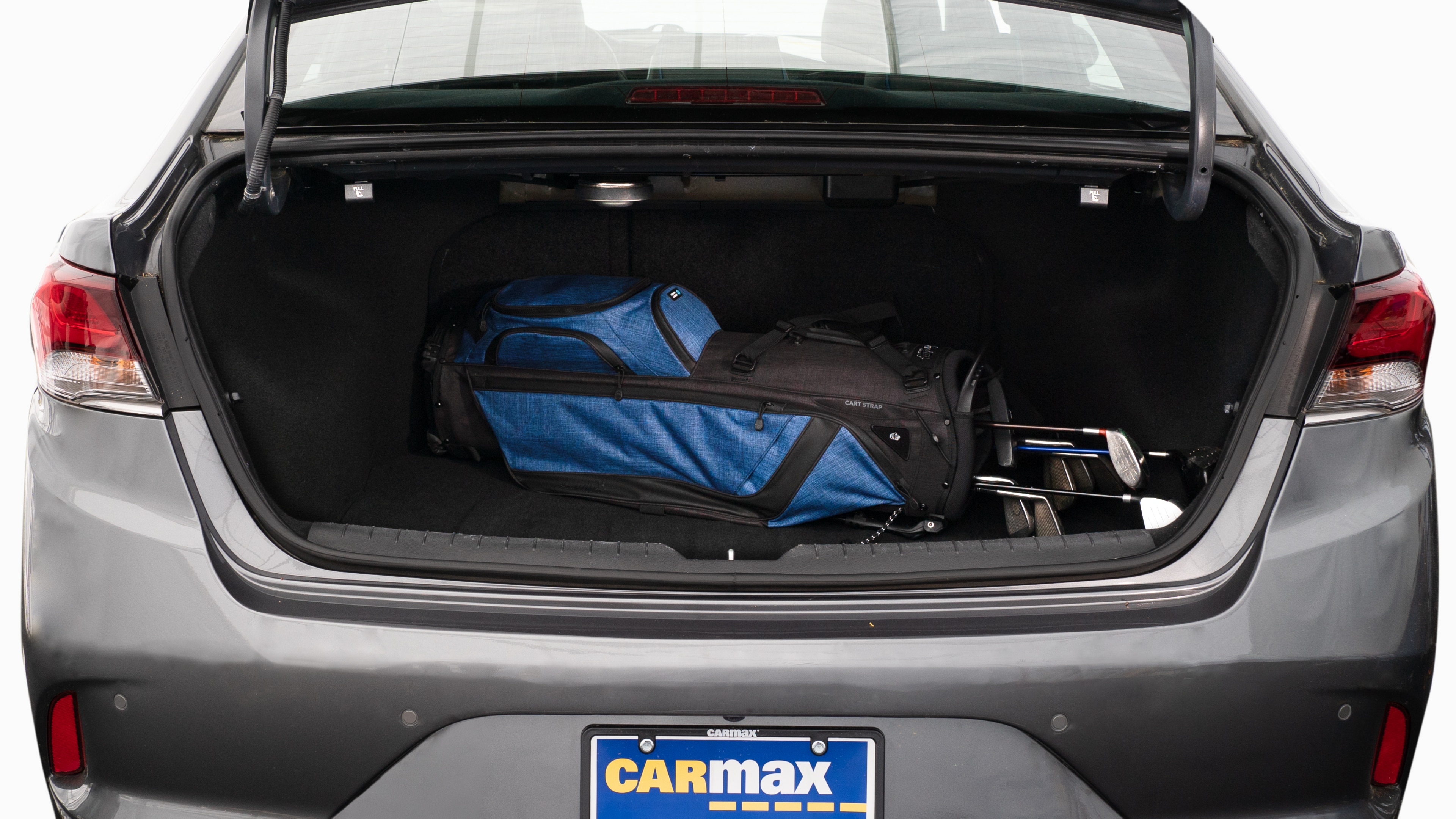 The trunk lid is open showing full view of the trunk. A baby stroller, two grocery carriers, two camping chairs in the carrying bag, and a set of golf clubs are placed inside.