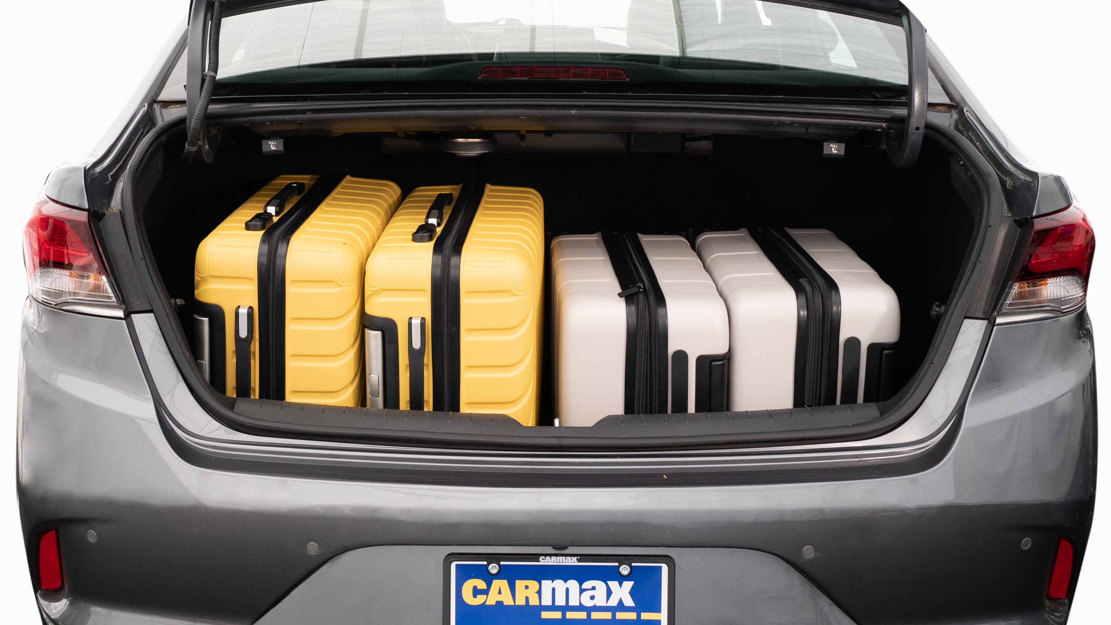The trunk lid is open, showing a full view of the trunk space. Two large and two small suitcases are placed on their sides.