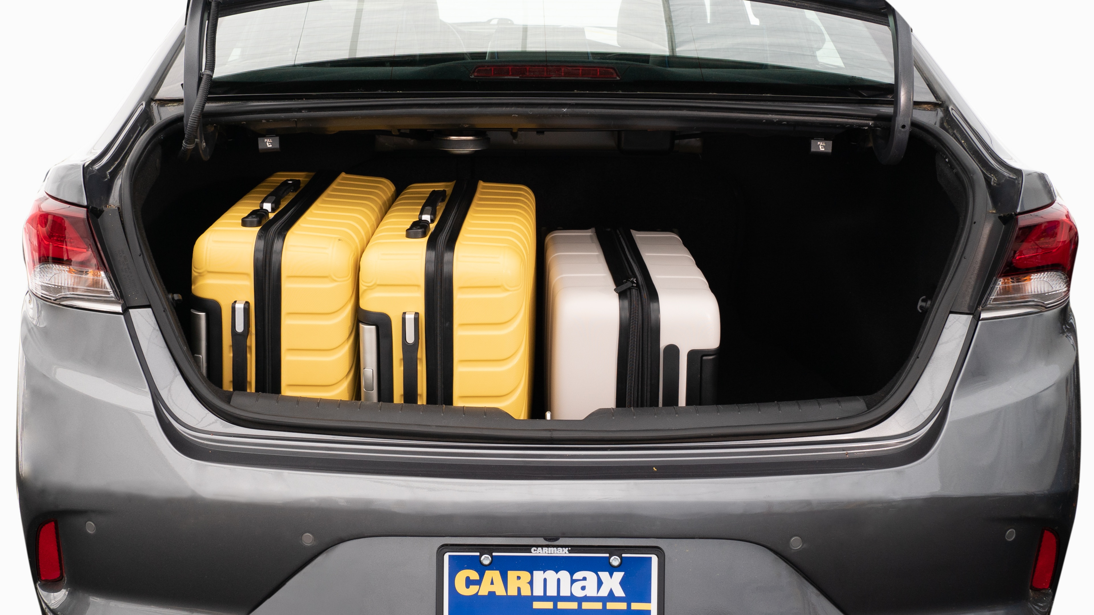 The trunk lid is open, showing a full view of the trunk space. Two large and two small suitcases are placed on their sides.