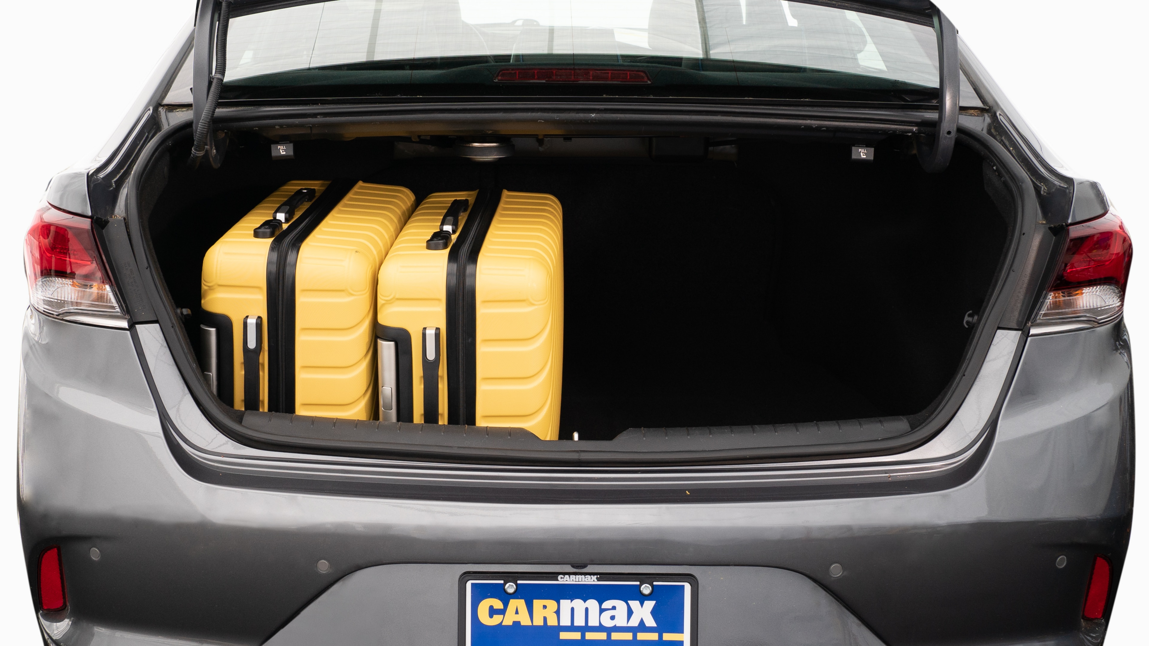 The trunk lid is open, showing a full view of the trunk space. Two large and two small suitcases are placed on their sides.