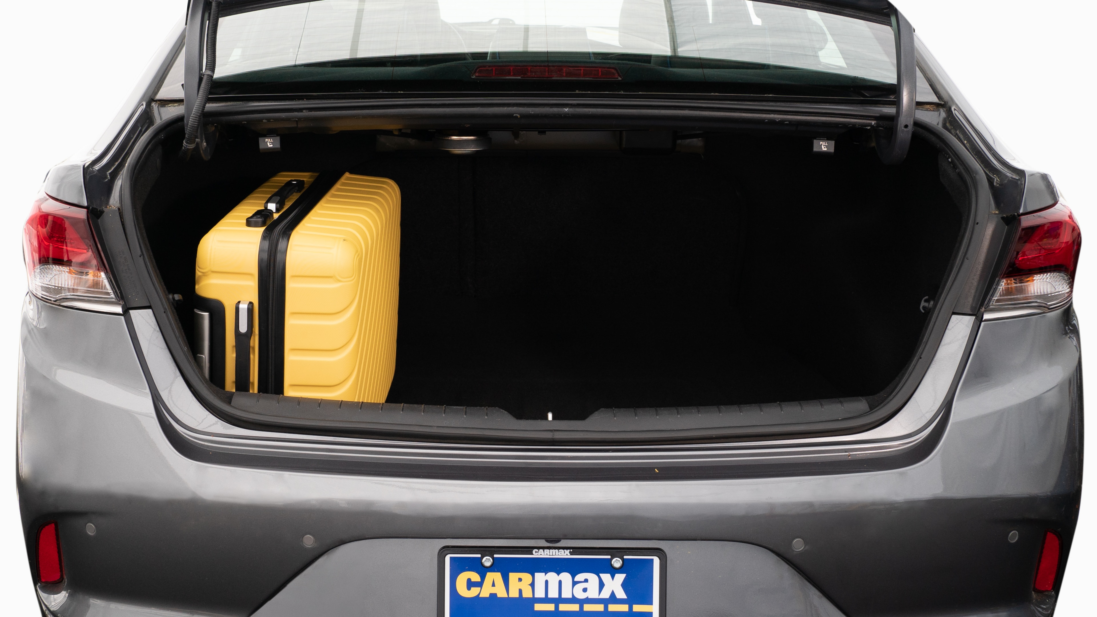 The trunk lid is open, showing a full view of the trunk space. Two large and two small suitcases are placed on their sides.
