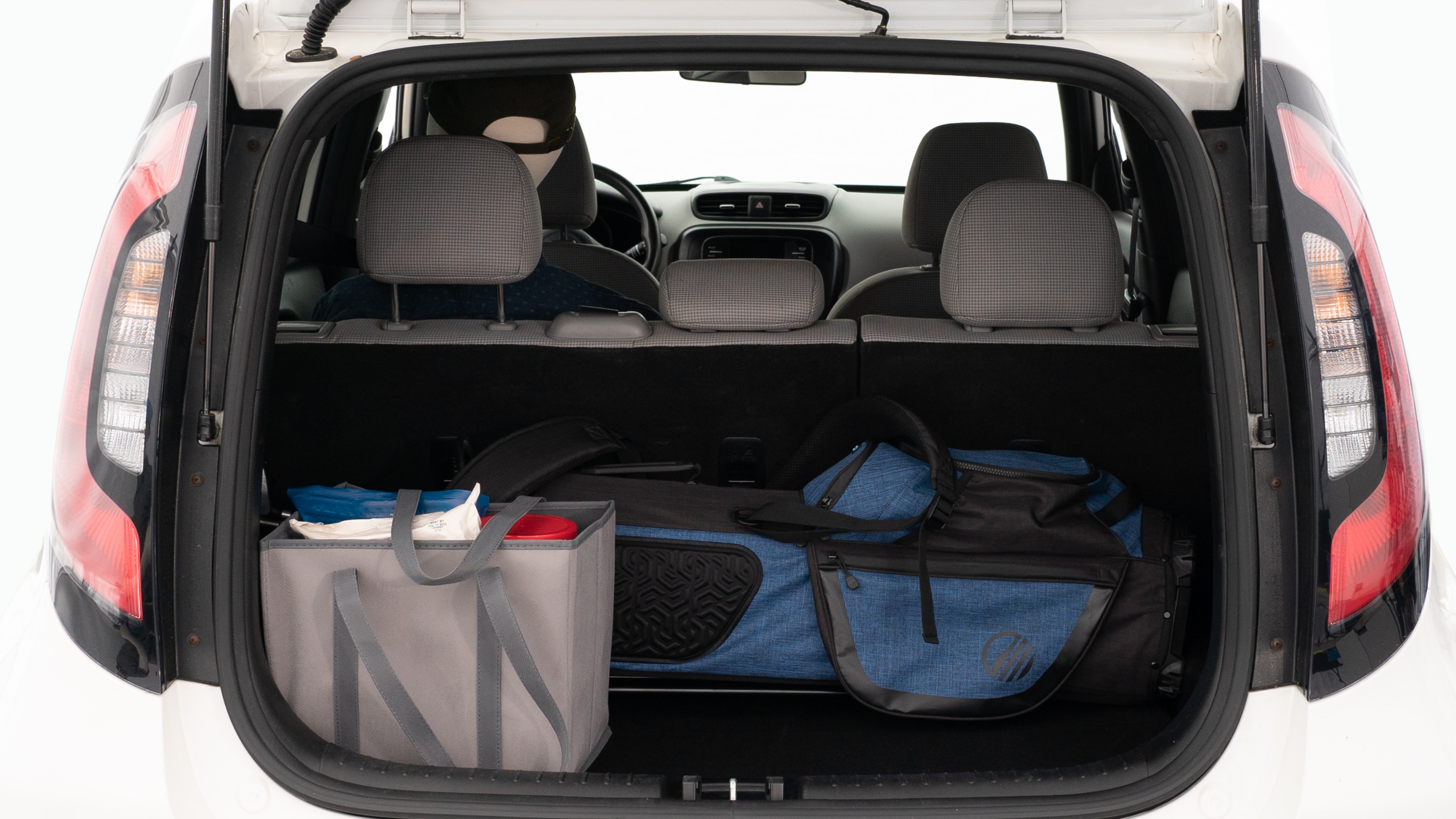 The trunk lid is open showing full view of the trunk. A baby stroller, three grocery carriers, and a set of golf clubs are placed inside.