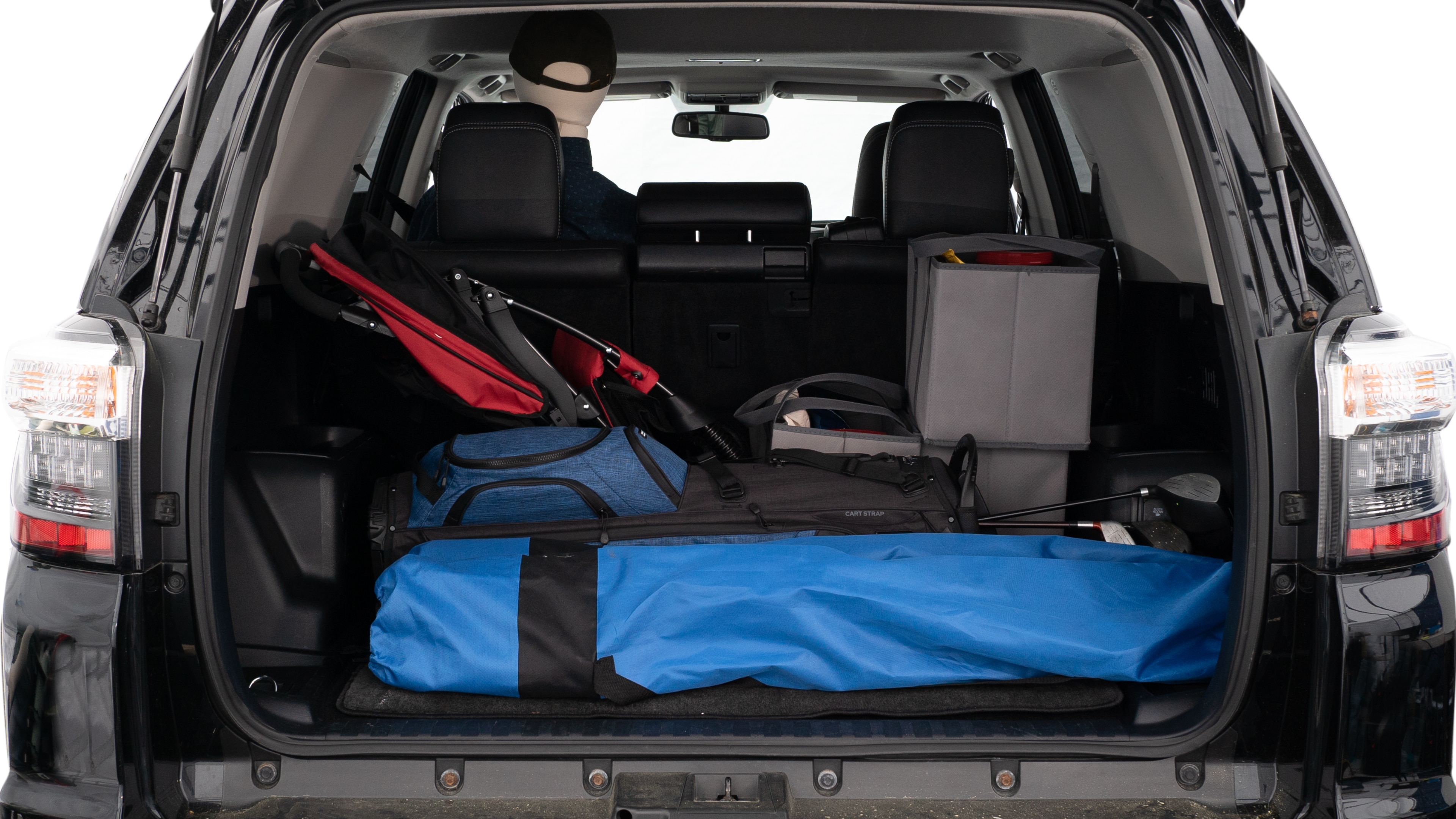 The trunk lid is open showing full view of the trunk. A baby stroller, three grocery carriers, two camping chairs in the carrying bag, and a set of golf clubs are placed inside.