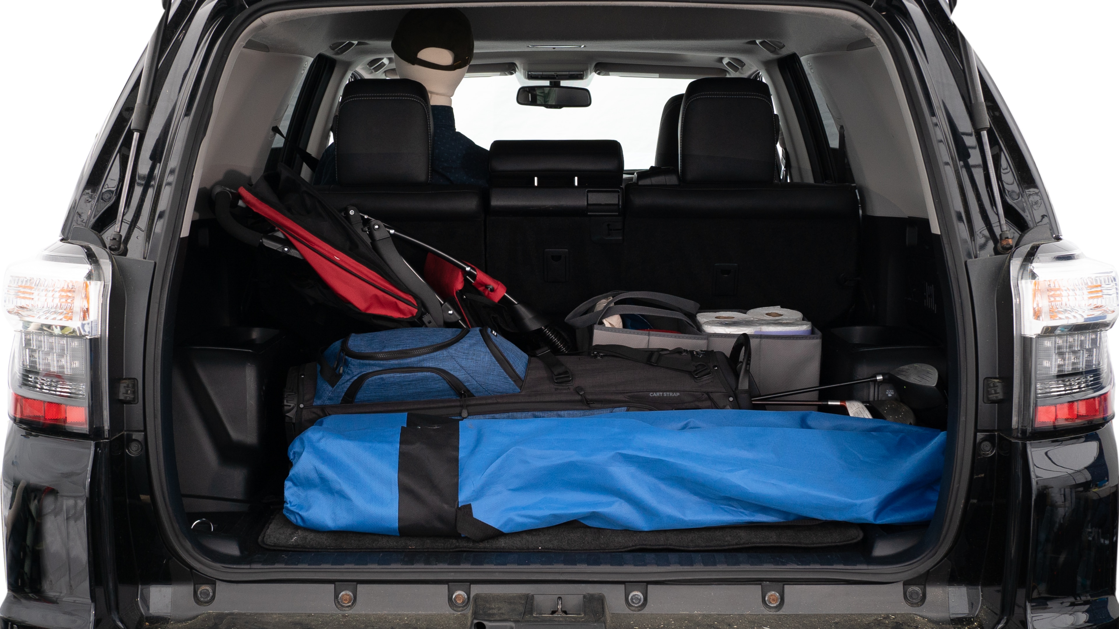 The trunk lid is open showing full view of the trunk. A baby stroller, three grocery carriers, two camping chairs in the carrying bag, and a set of golf clubs are placed inside.