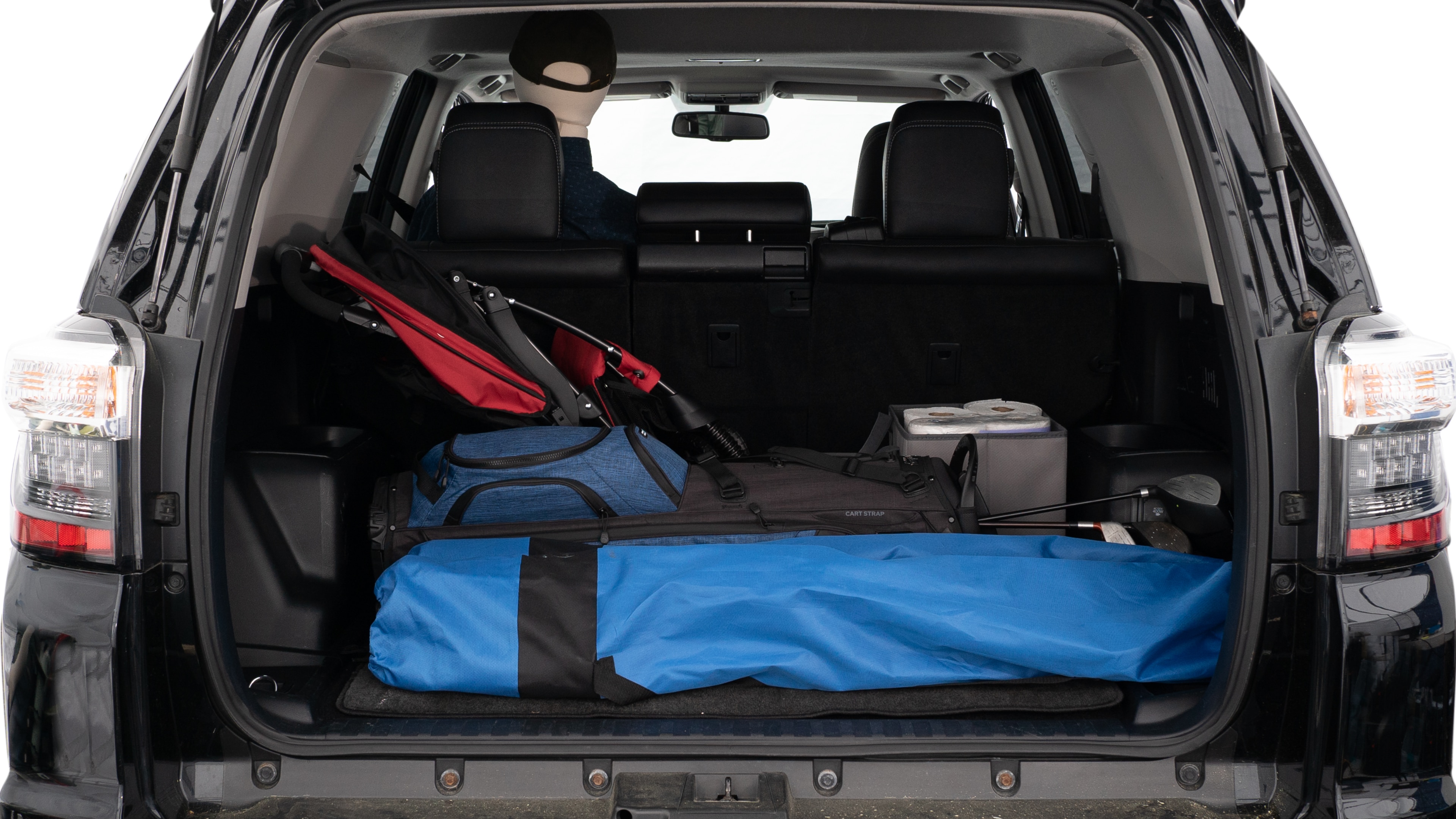 The trunk lid is open showing full view of the trunk. A baby stroller, three grocery carriers, two camping chairs in the carrying bag, and a set of golf clubs are placed inside.