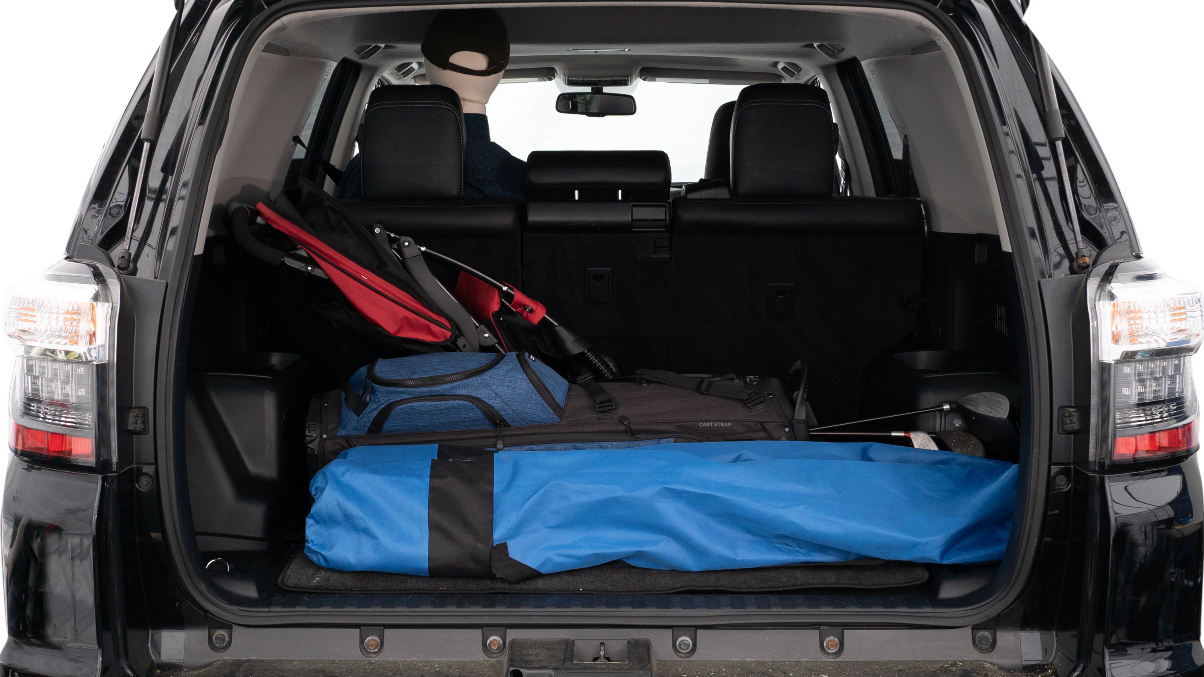 The trunk lid is open showing full view of the trunk. A baby stroller, three grocery carriers, two camping chairs in the carrying bag, and a set of golf clubs are placed inside.