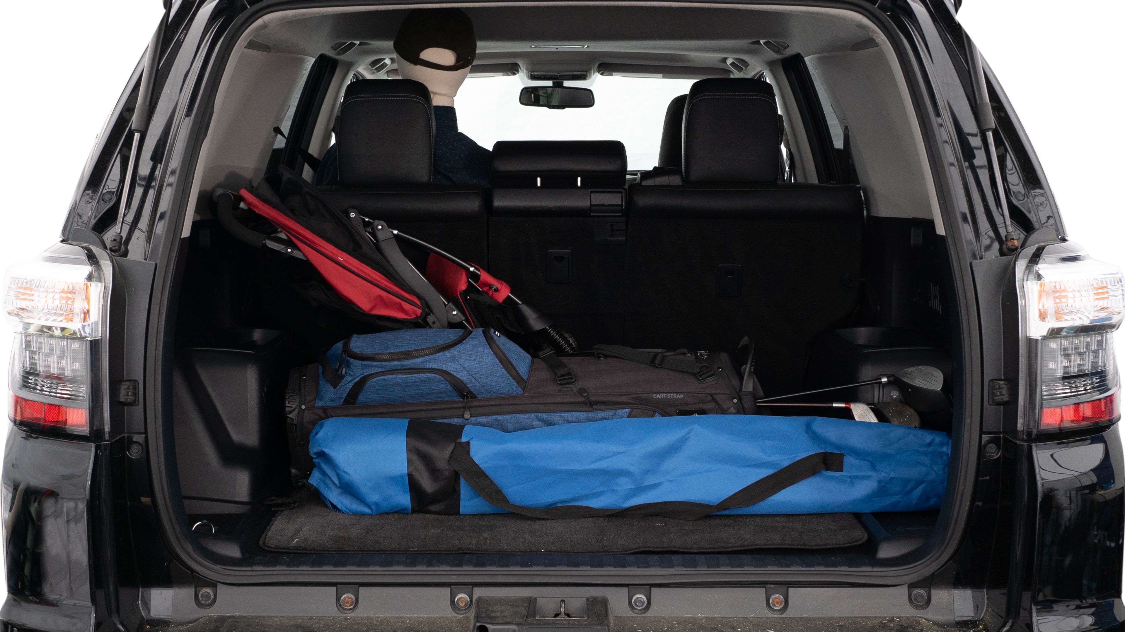 The trunk lid is open showing full view of the trunk. A baby stroller, three grocery carriers, two camping chairs in the carrying bag, and a set of golf clubs are placed inside.
