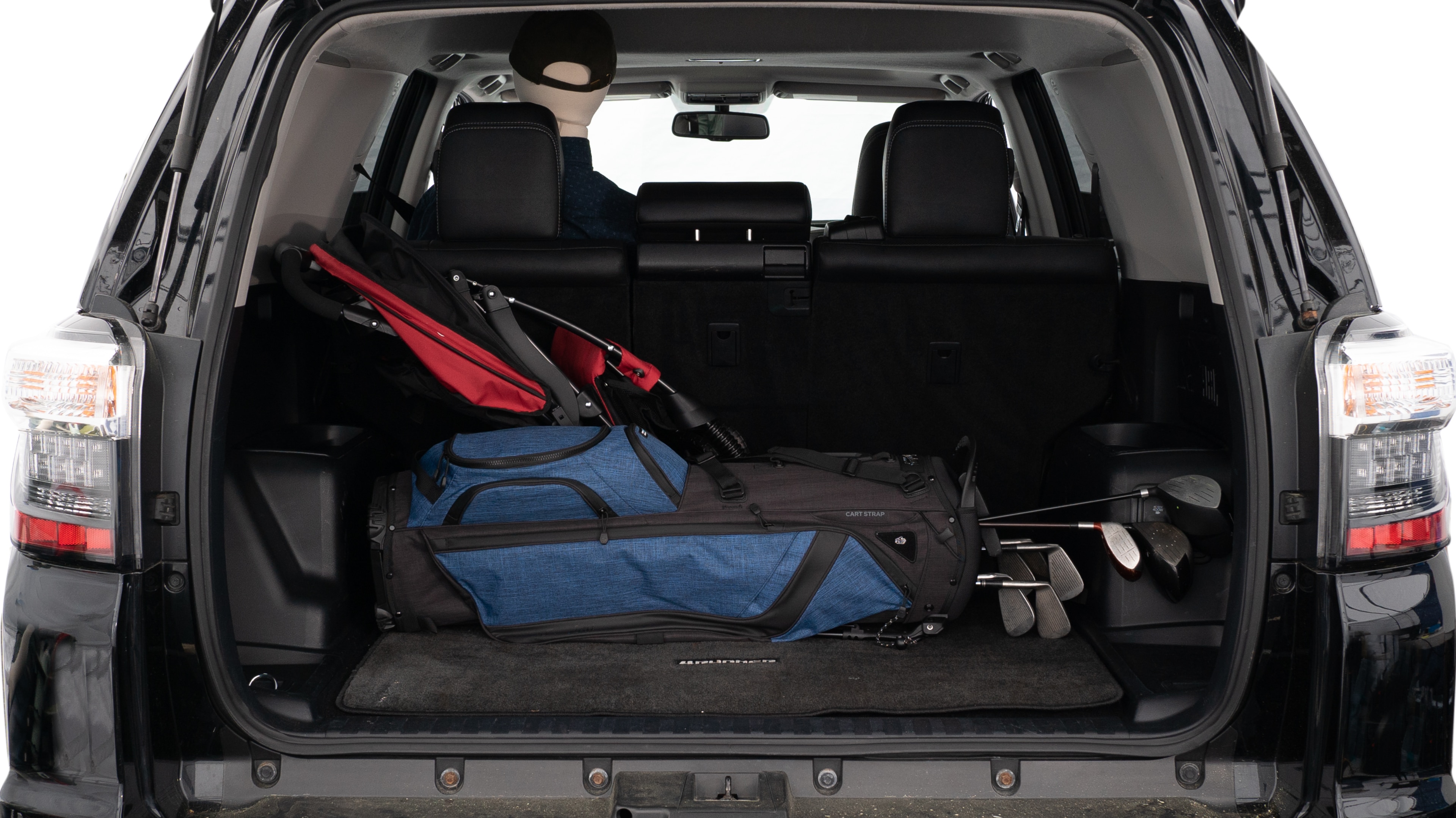 The trunk lid is open showing full view of the trunk. A baby stroller, three grocery carriers, two camping chairs in the carrying bag, and a set of golf clubs are placed inside.