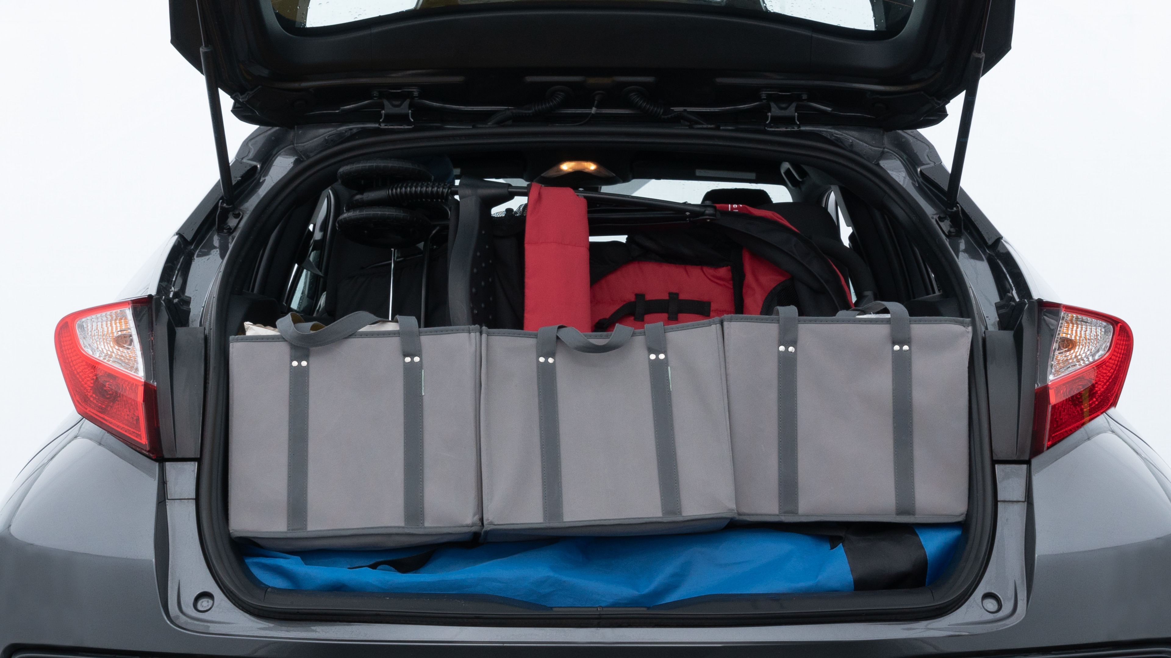 The trunk lid is open showing full view of the trunk. A baby stroller, three grocery carriers, two camping chairs in the carrying bag, and a set of golf clubs are placed inside.