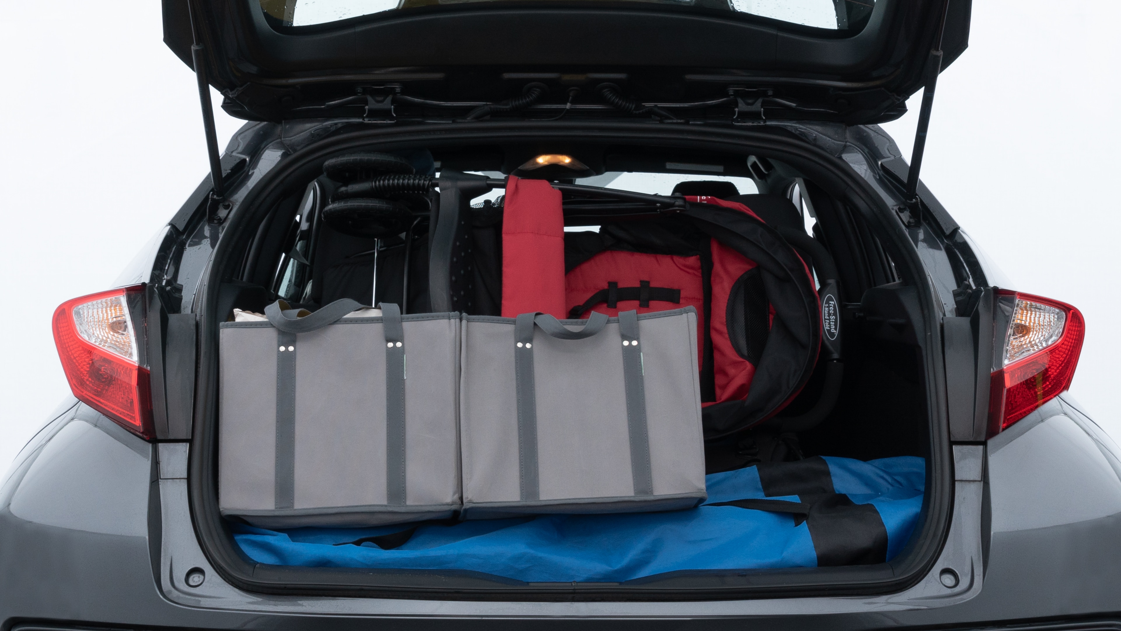 The trunk lid is open showing full view of the trunk. A baby stroller, three grocery carriers, two camping chairs in the carrying bag, and a set of golf clubs are placed inside.