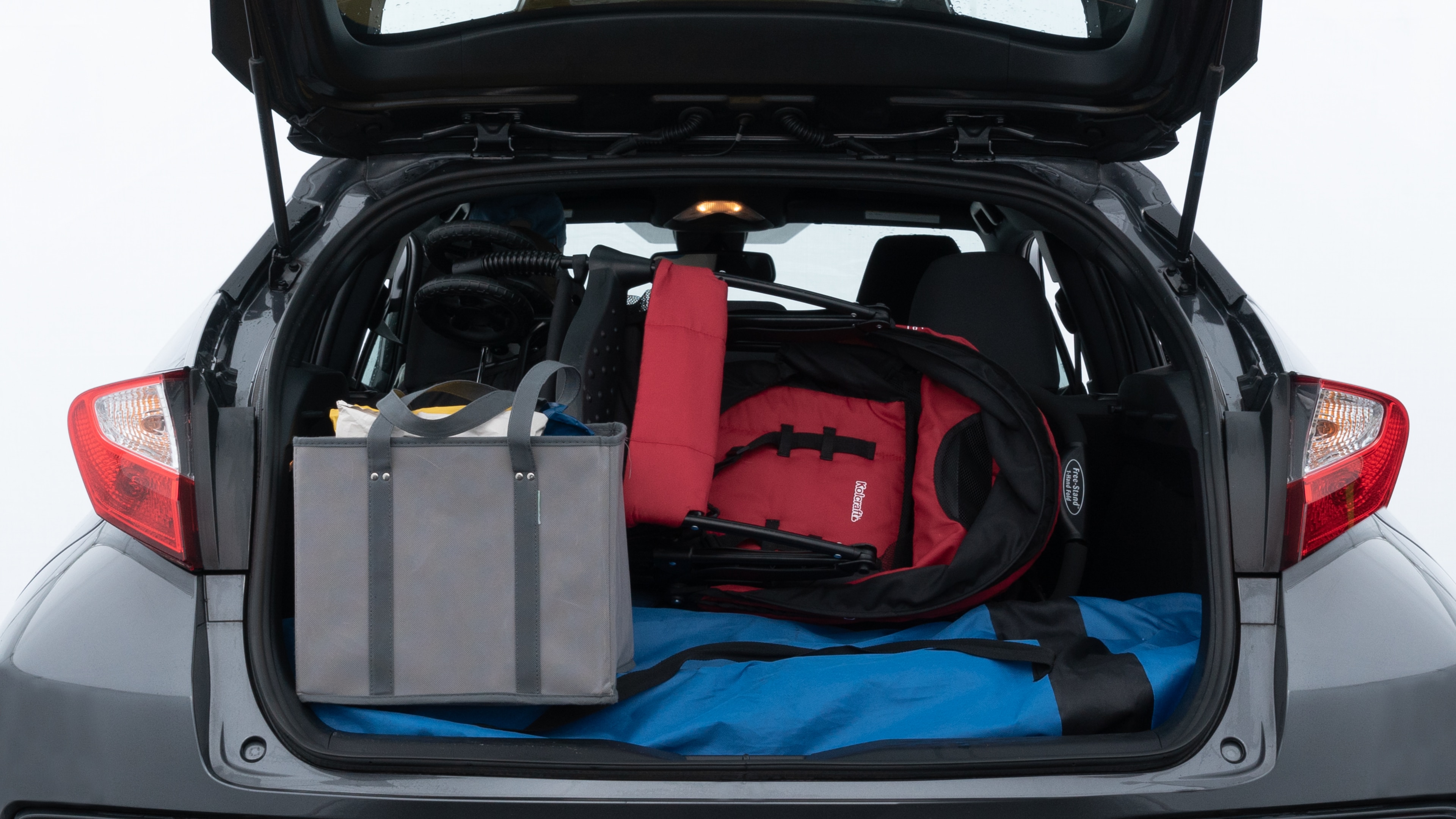 The trunk lid is open showing full view of the trunk. A baby stroller, three grocery carriers, two camping chairs in the carrying bag, and a set of golf clubs are placed inside.
