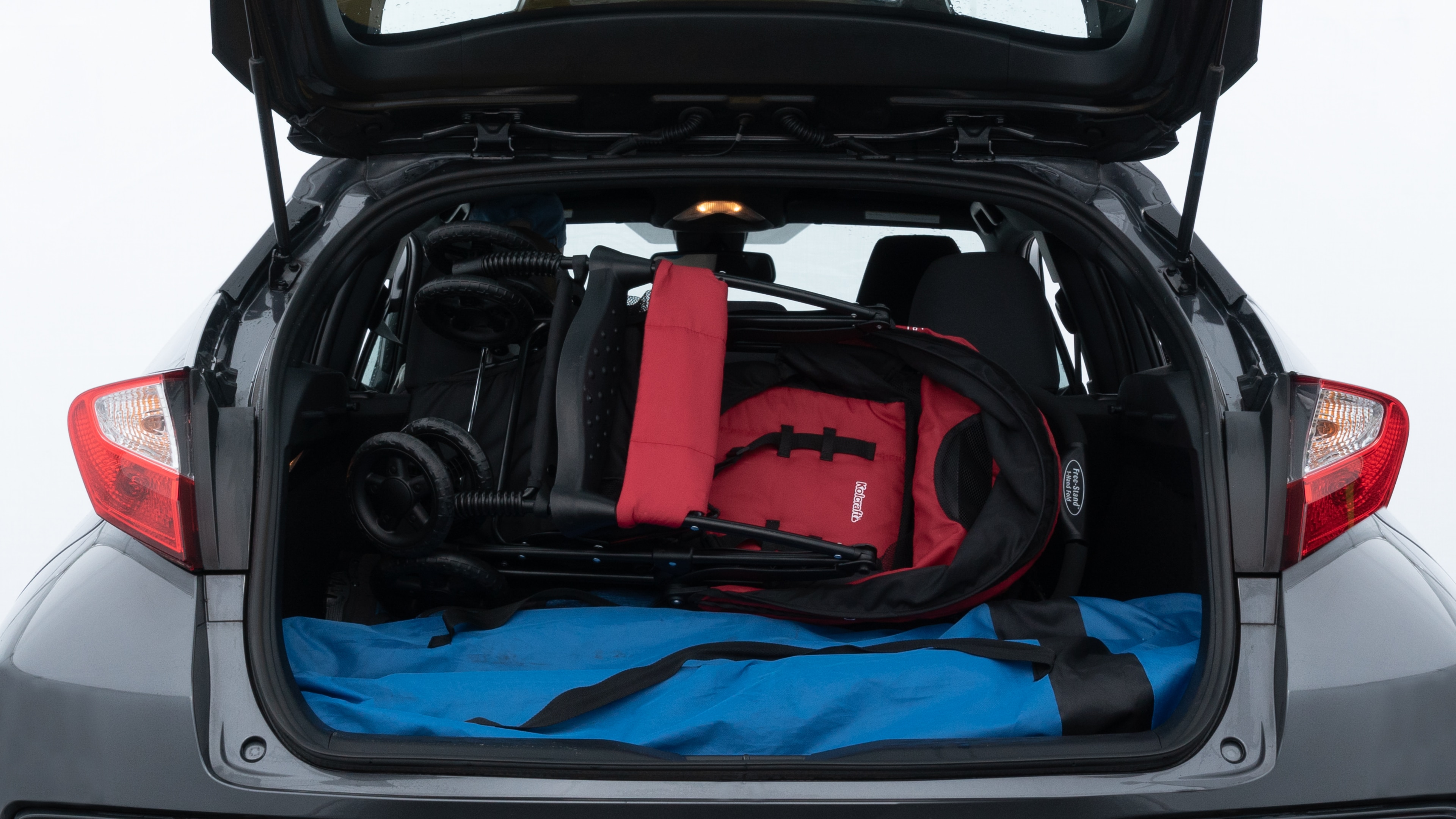 The trunk lid is open showing full view of the trunk. A baby stroller, three grocery carriers, two camping chairs in the carrying bag, and a set of golf clubs are placed inside.