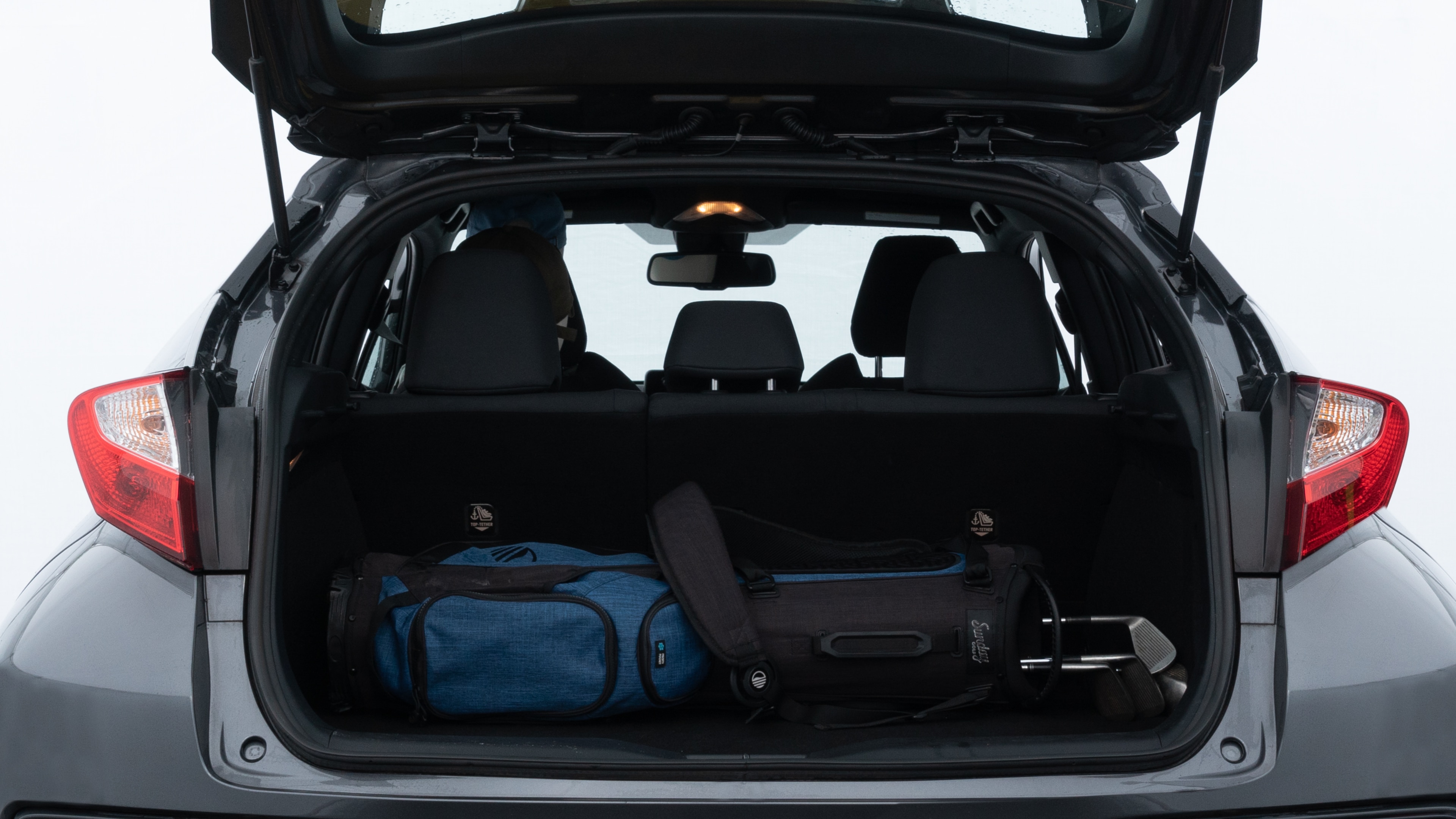 The trunk lid is open showing full view of the trunk. A baby stroller, three grocery carriers, two camping chairs in the carrying bag, and a set of golf clubs are placed inside.