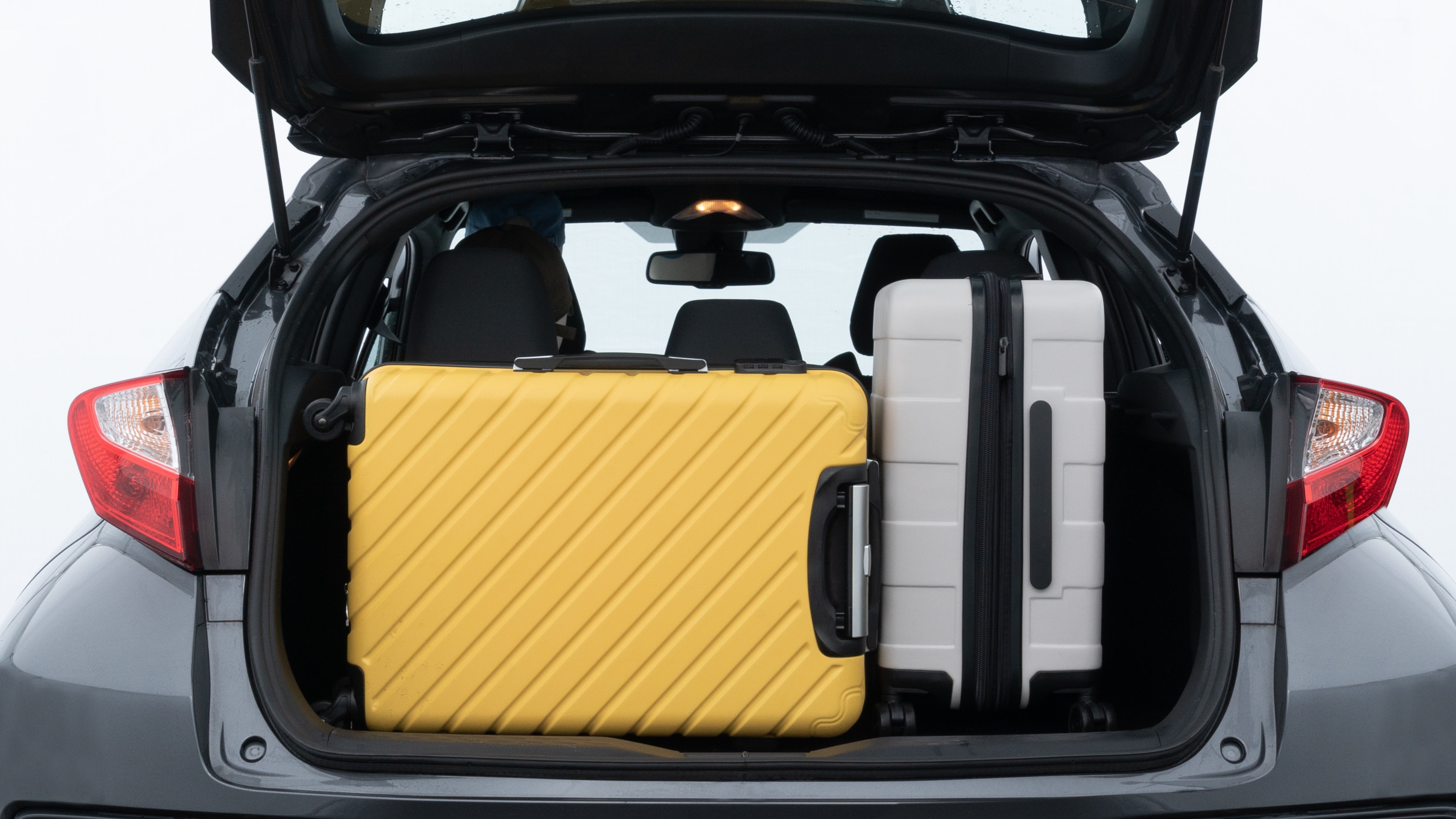 The trunk lid is open, showing full view of the trunk space. Two medium and one small suitcases are placed inside.