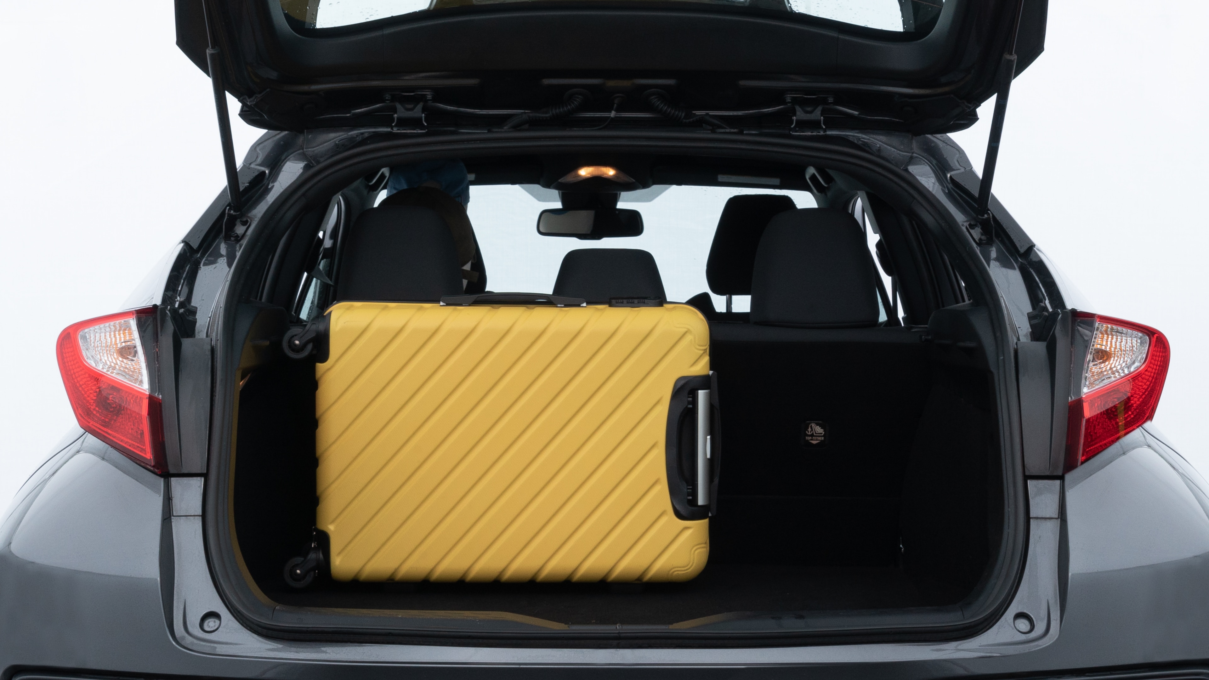 The trunk lid is open, showing full view of the trunk space. Two medium and one small suitcases are placed inside.