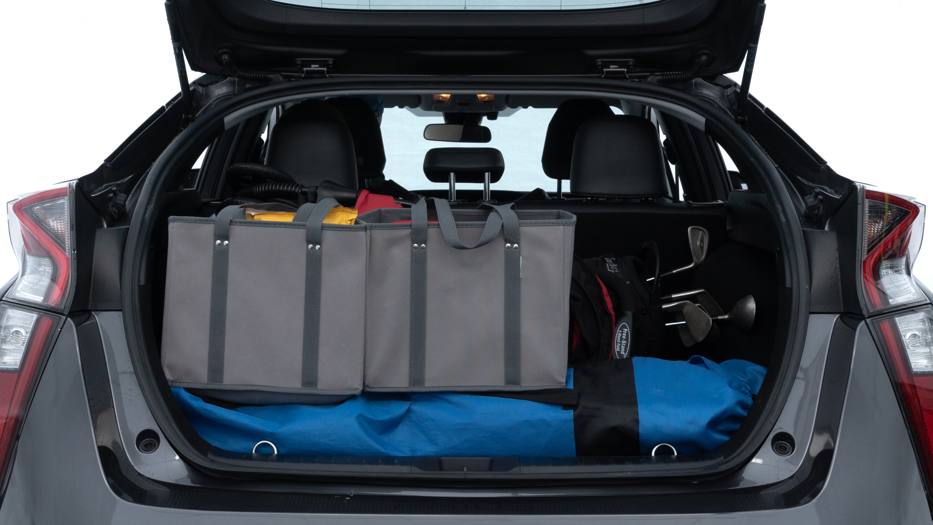 The trunk lid is open showing full view of the trunk. A baby stroller, three grocery carriers, two camping chairs in the carrying bag, and a set of golf clubs are placed inside.