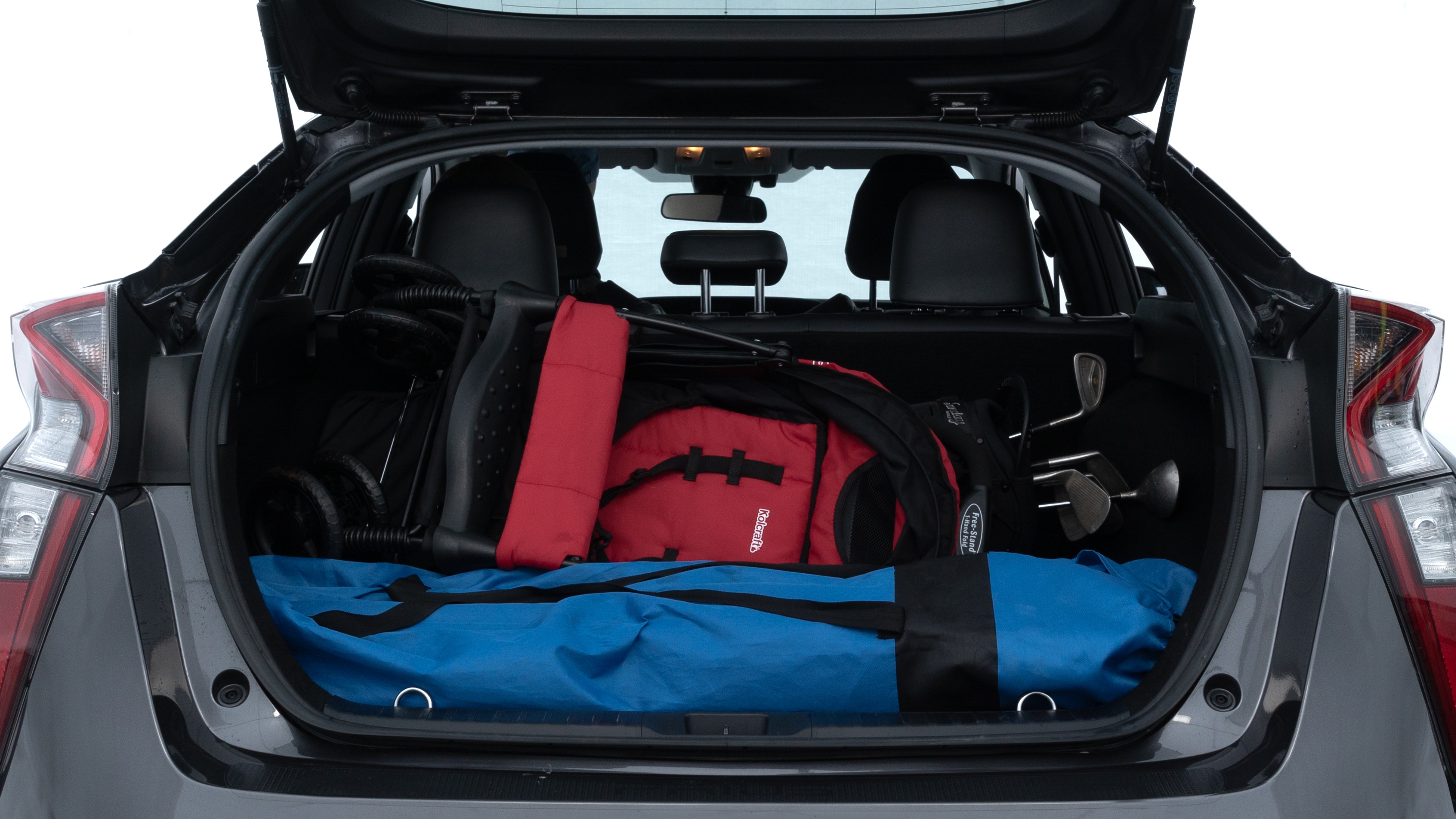 The trunk lid is open showing full view of the trunk. A baby stroller, three grocery carriers, two camping chairs in the carrying bag, and a set of golf clubs are placed inside.