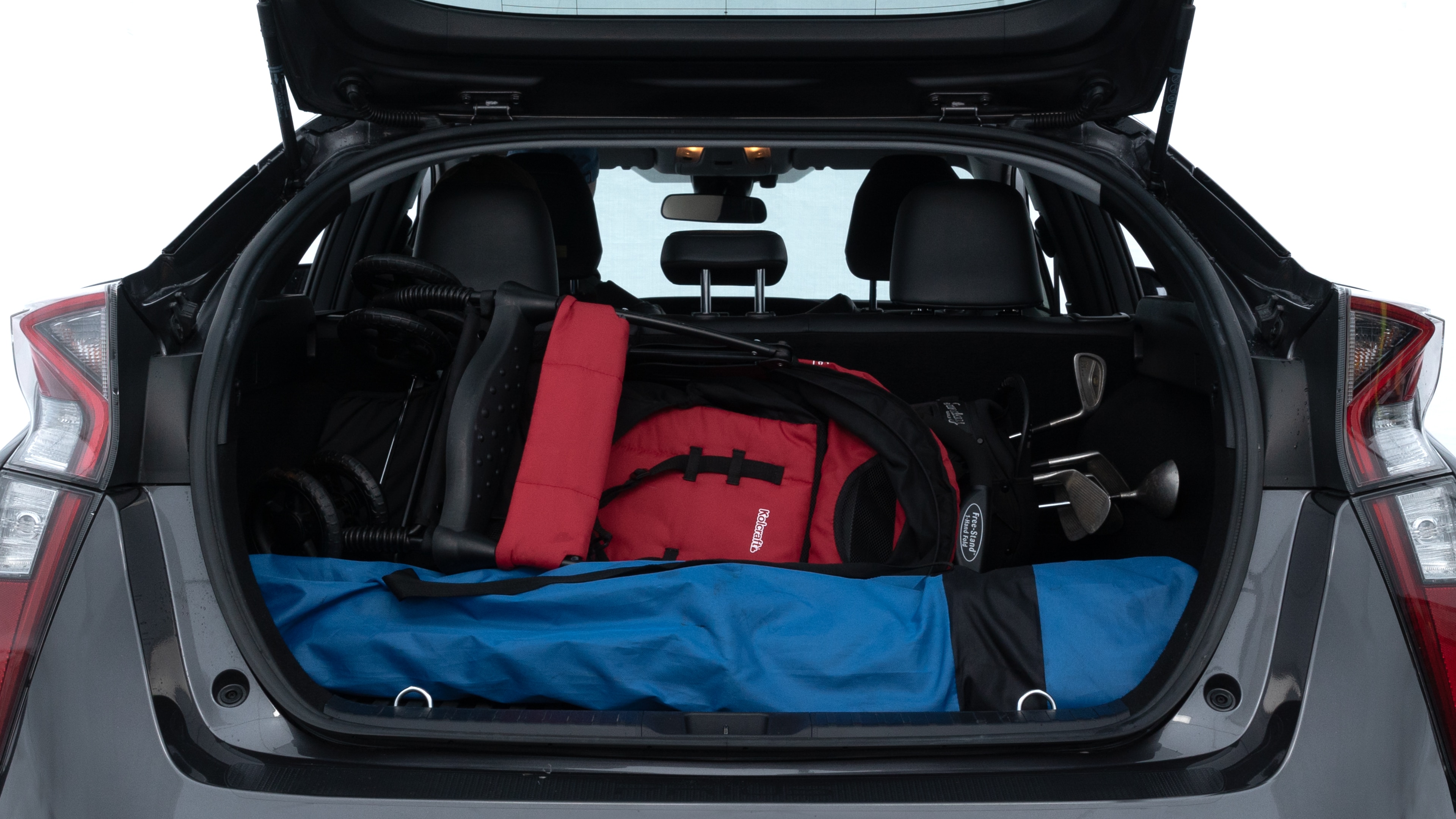 The trunk lid is open showing full view of the trunk. A baby stroller, three grocery carriers, two camping chairs in the carrying bag, and a set of golf clubs are placed inside.