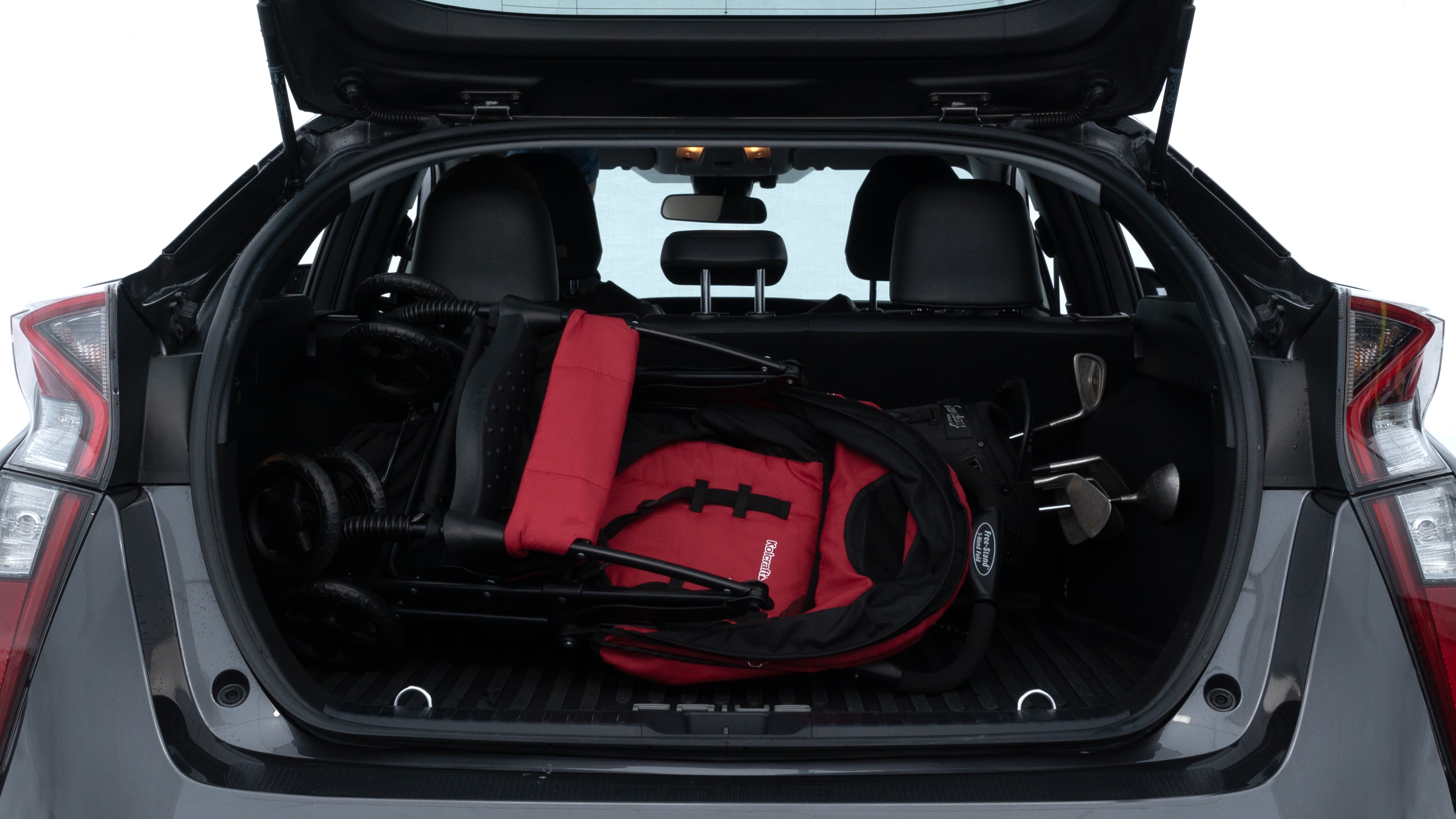 The trunk lid is open showing full view of the trunk. A baby stroller, three grocery carriers, two camping chairs in the carrying bag, and a set of golf clubs are placed inside.
