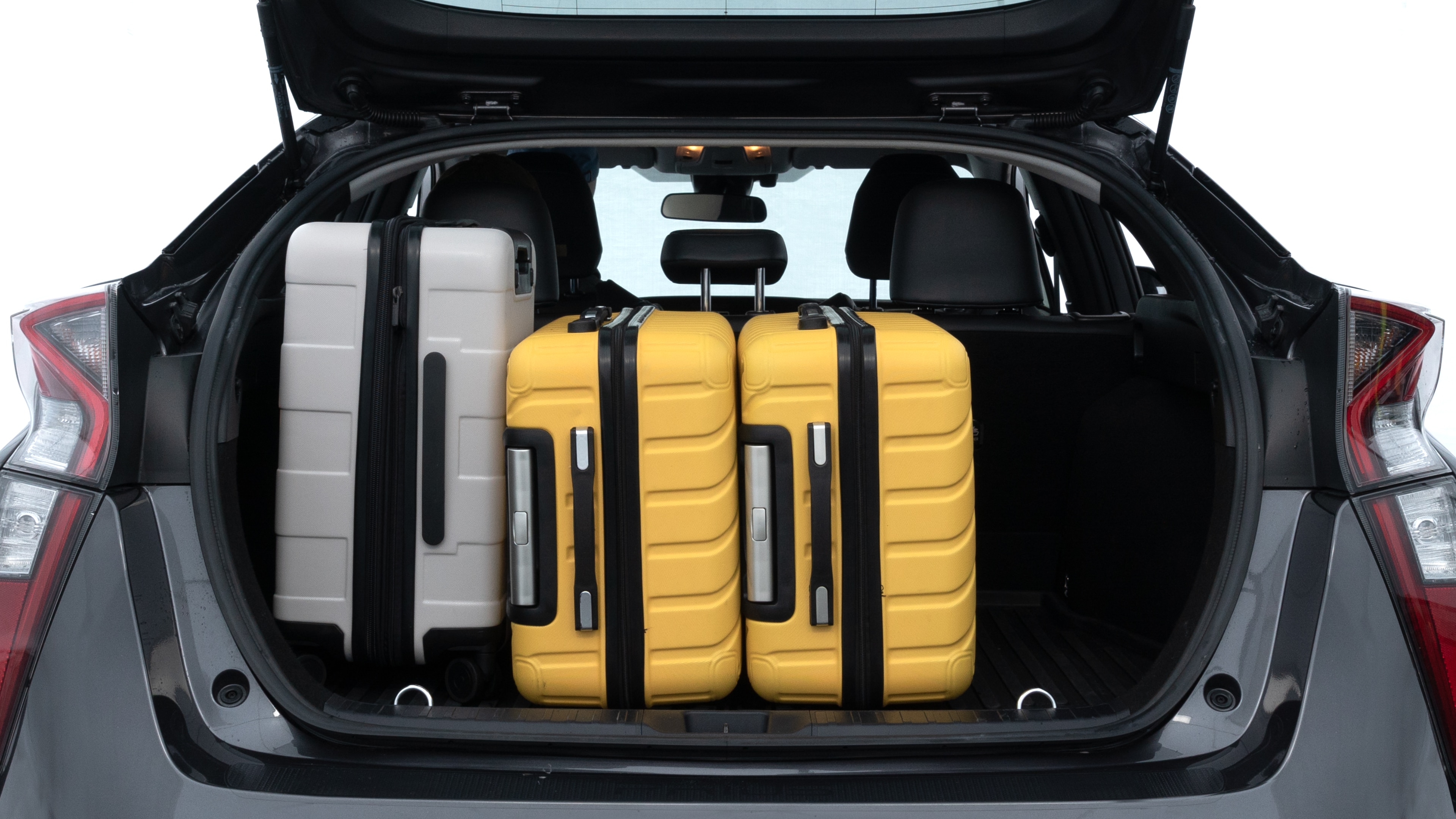 The trunk lid is open, showing full view of the trunk space. Two medium and two small suitcases are placed inside.