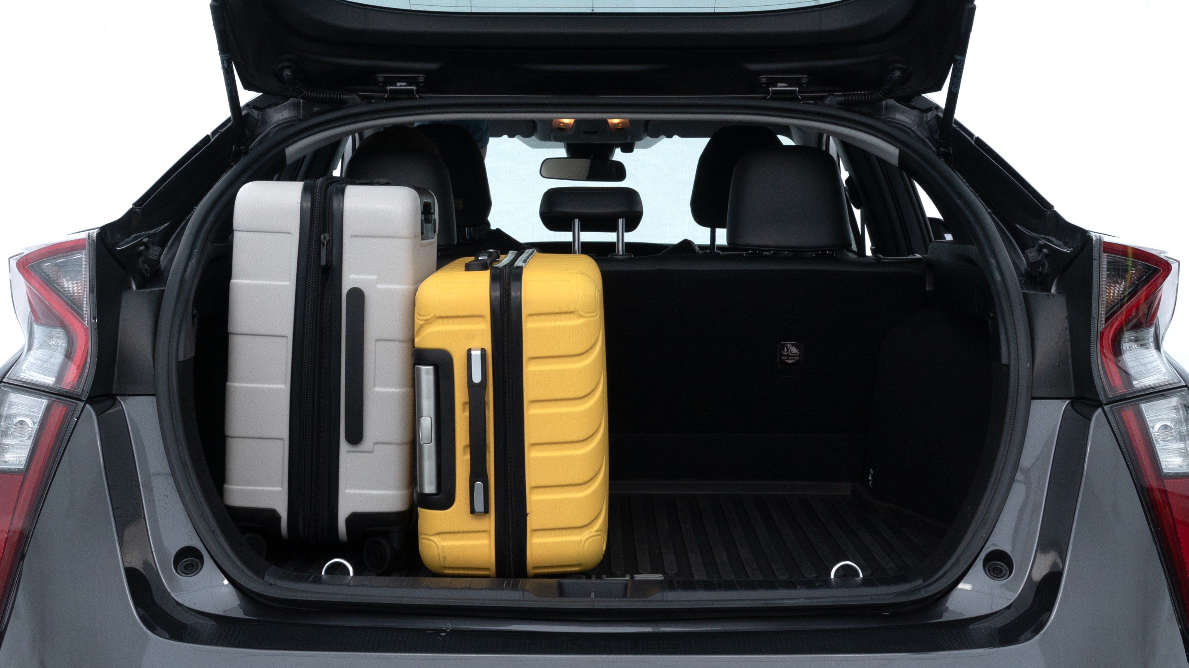 The trunk lid is open, showing full view of the trunk space. Two medium and two small suitcases are placed inside.