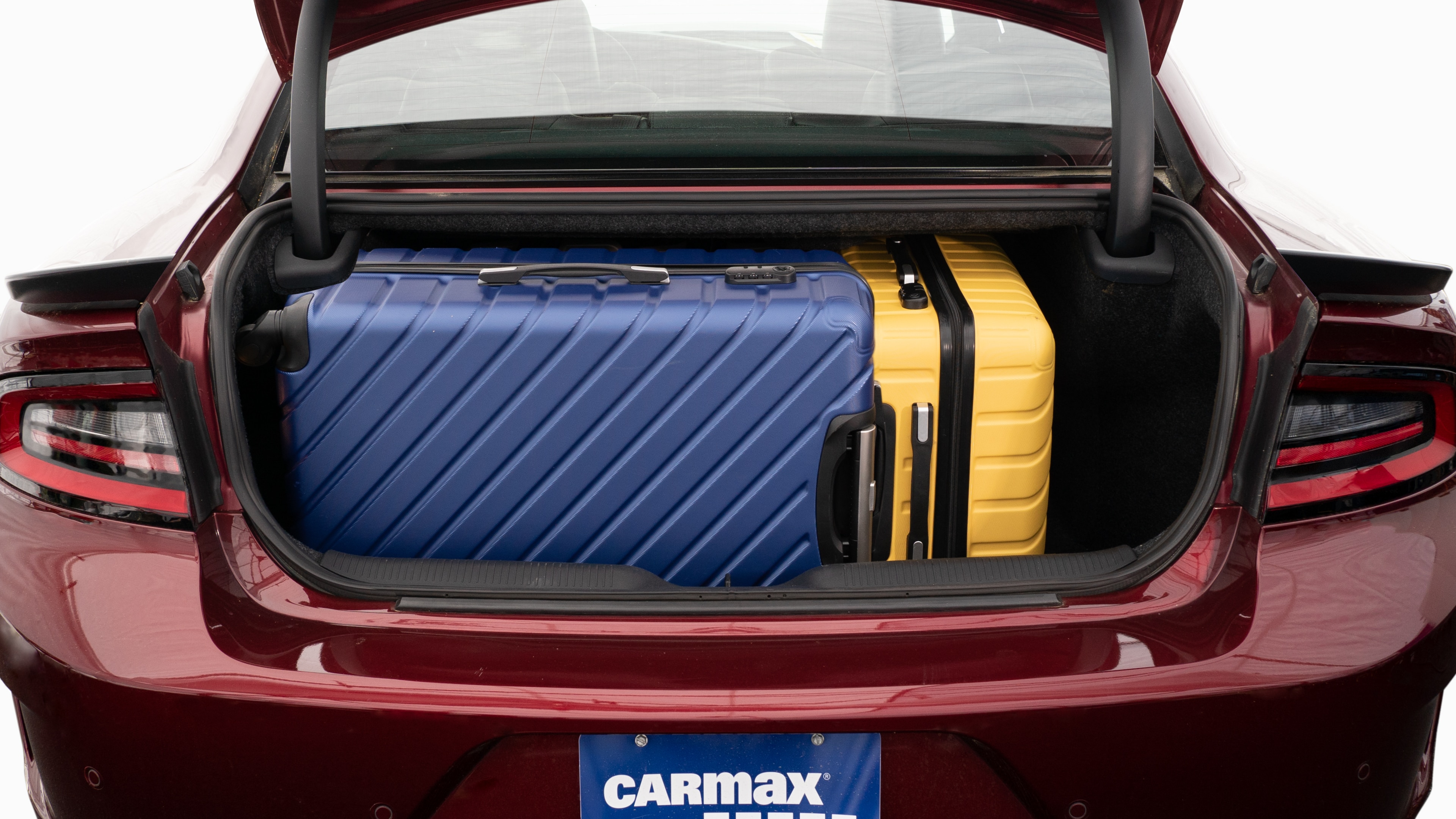 The trunk lid is open, showing full view of the trunk space. Two large and two small suitcases are placed inside.
