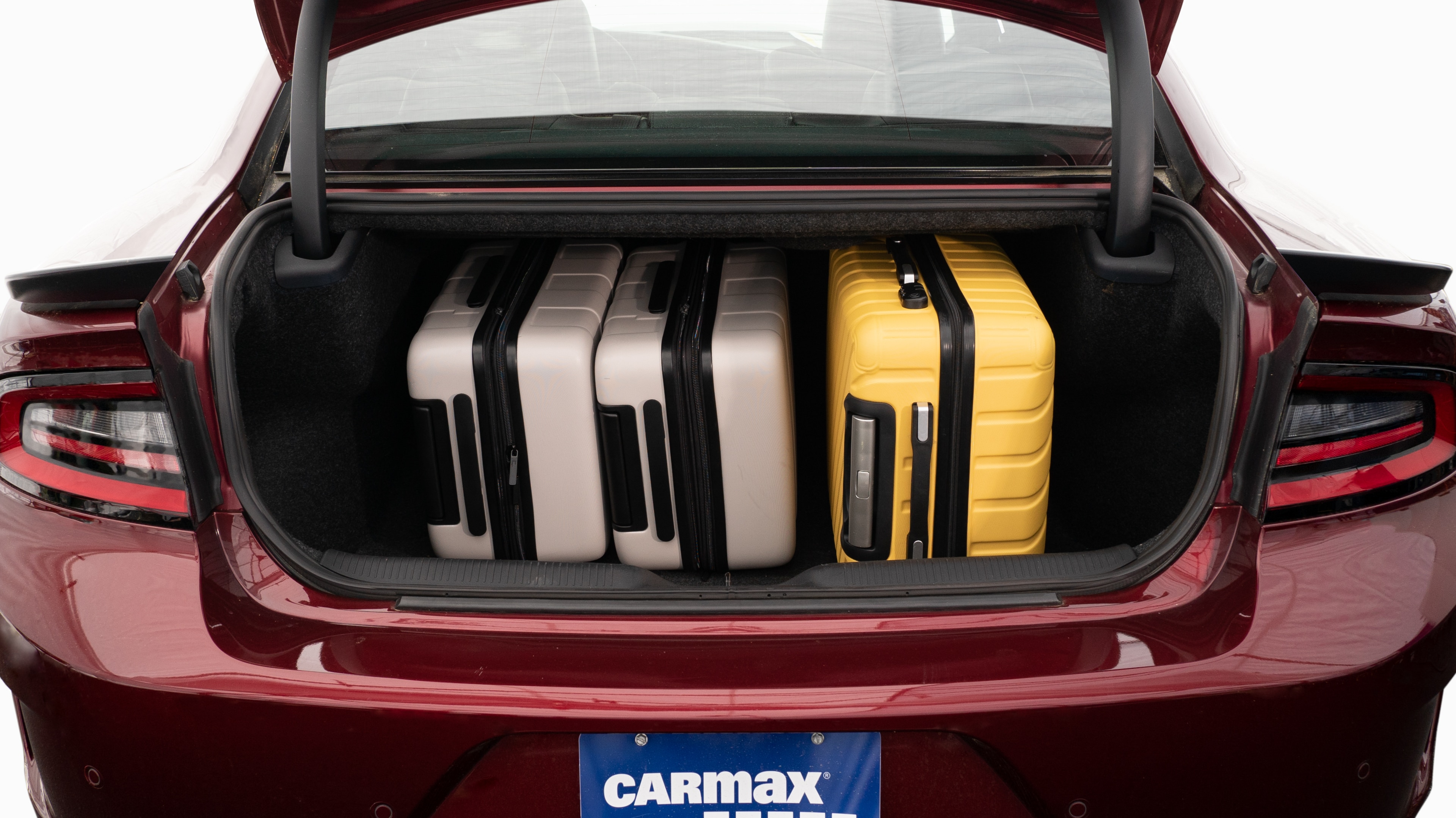 The trunk lid is open, showing full view of the trunk space. Two large and two small suitcases are placed inside.