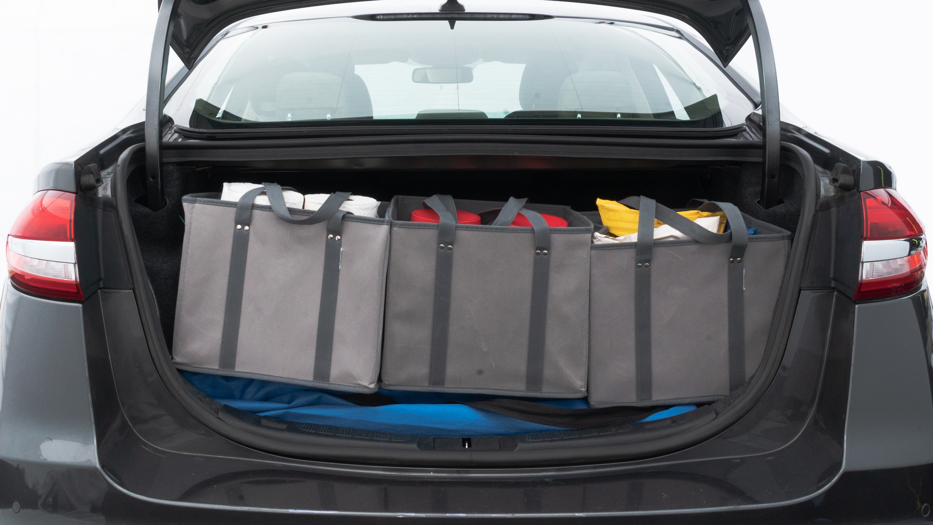 The trunk lid is open showing full view of the trunk. A baby stroller, three grocery carriers, two camping chairs in the carrying bag, and a set of golf clubs are placed inside.