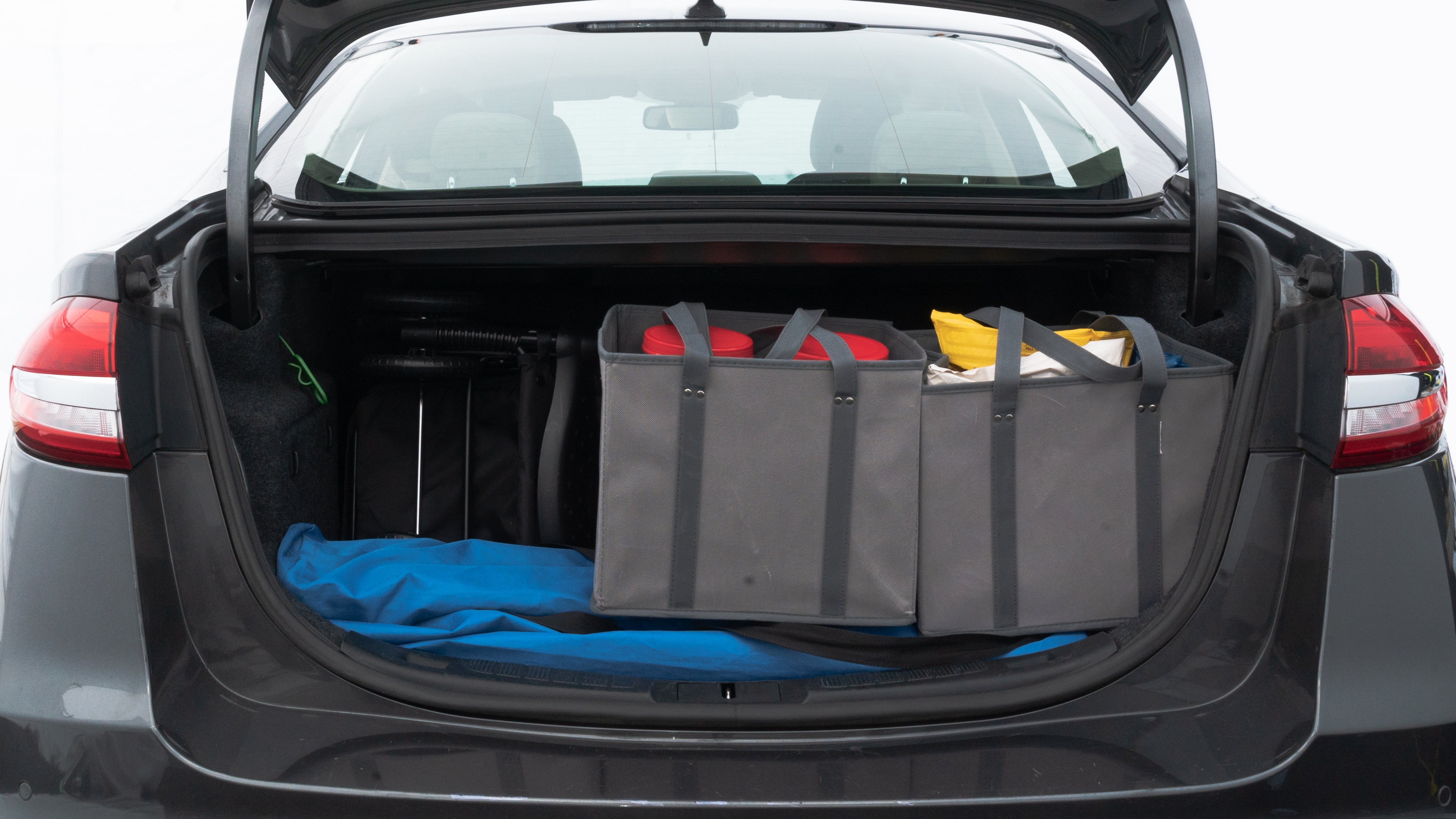The trunk lid is open showing full view of the trunk. A baby stroller, three grocery carriers, two camping chairs in the carrying bag, and a set of golf clubs are placed inside.