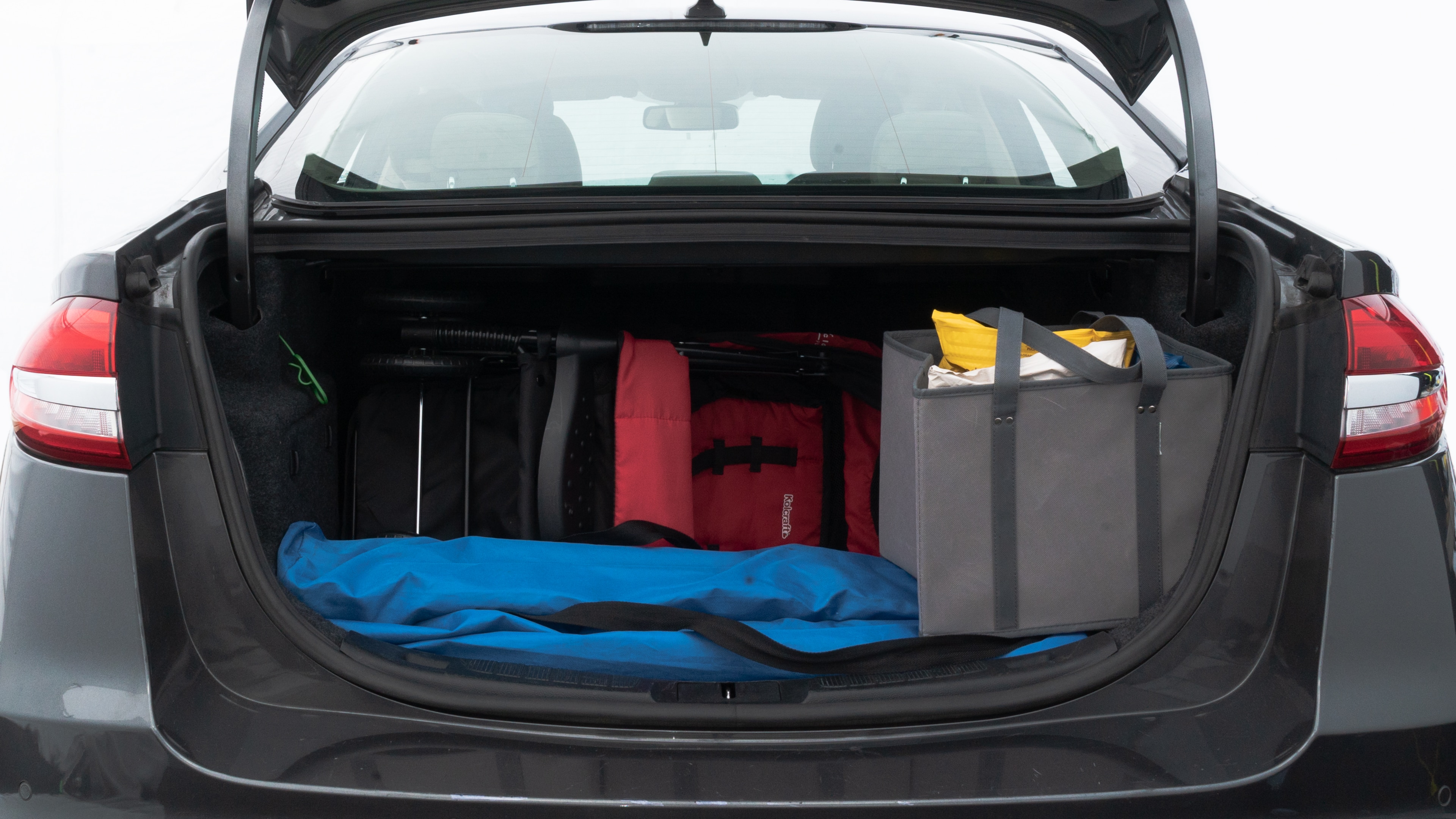 The trunk lid is open showing full view of the trunk. A baby stroller, three grocery carriers, two camping chairs in the carrying bag, and a set of golf clubs are placed inside.