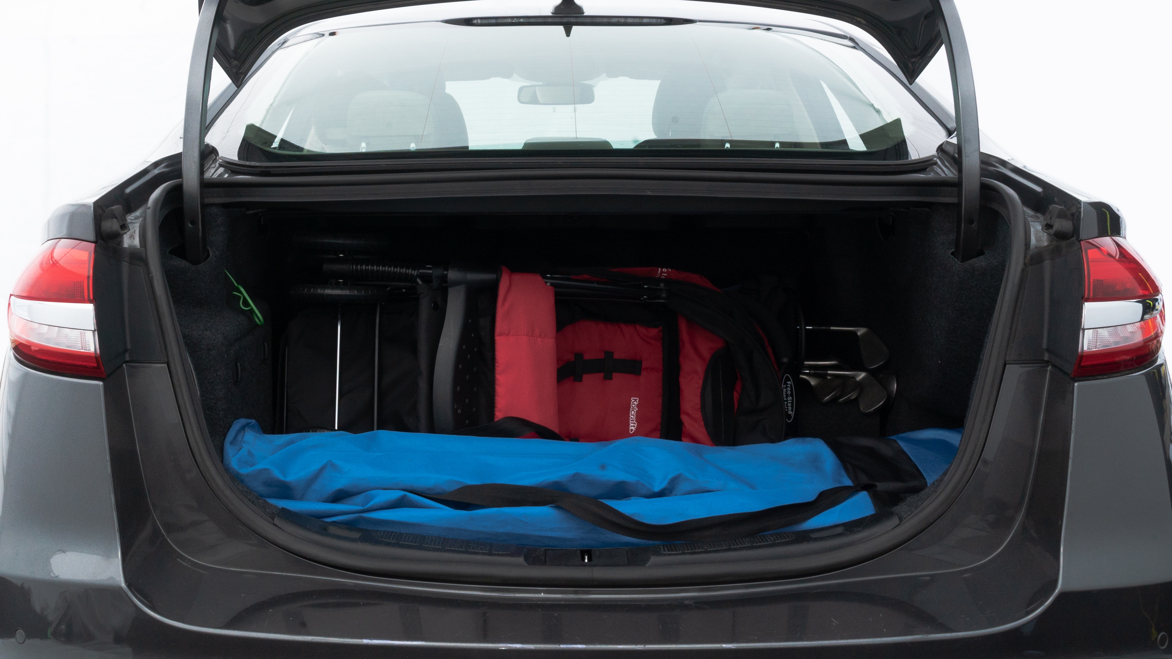 The trunk lid is open showing full view of the trunk. A baby stroller, three grocery carriers, two camping chairs in the carrying bag, and a set of golf clubs are placed inside.
