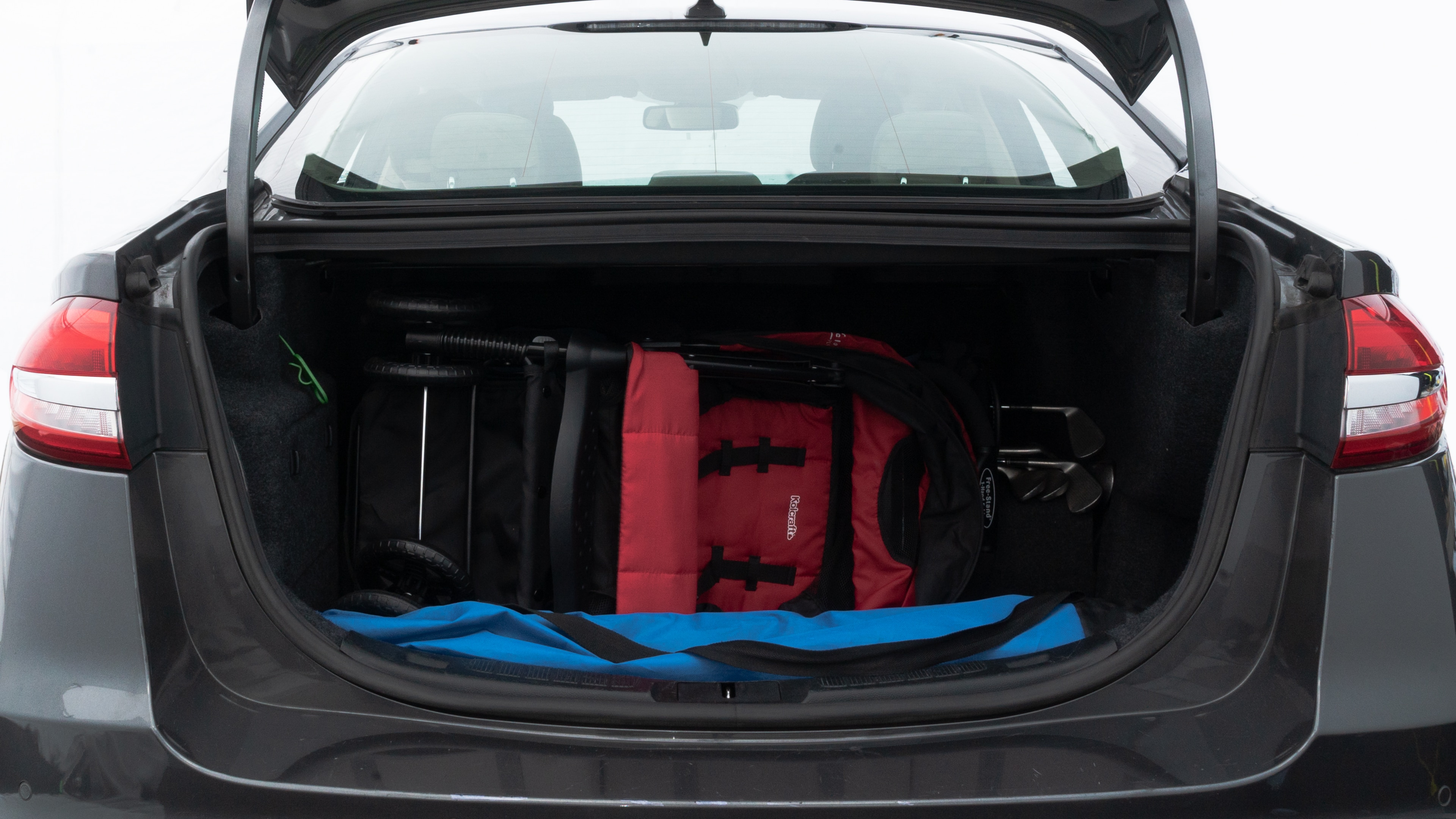 The trunk lid is open showing full view of the trunk. A baby stroller, three grocery carriers, two camping chairs in the carrying bag, and a set of golf clubs are placed inside.