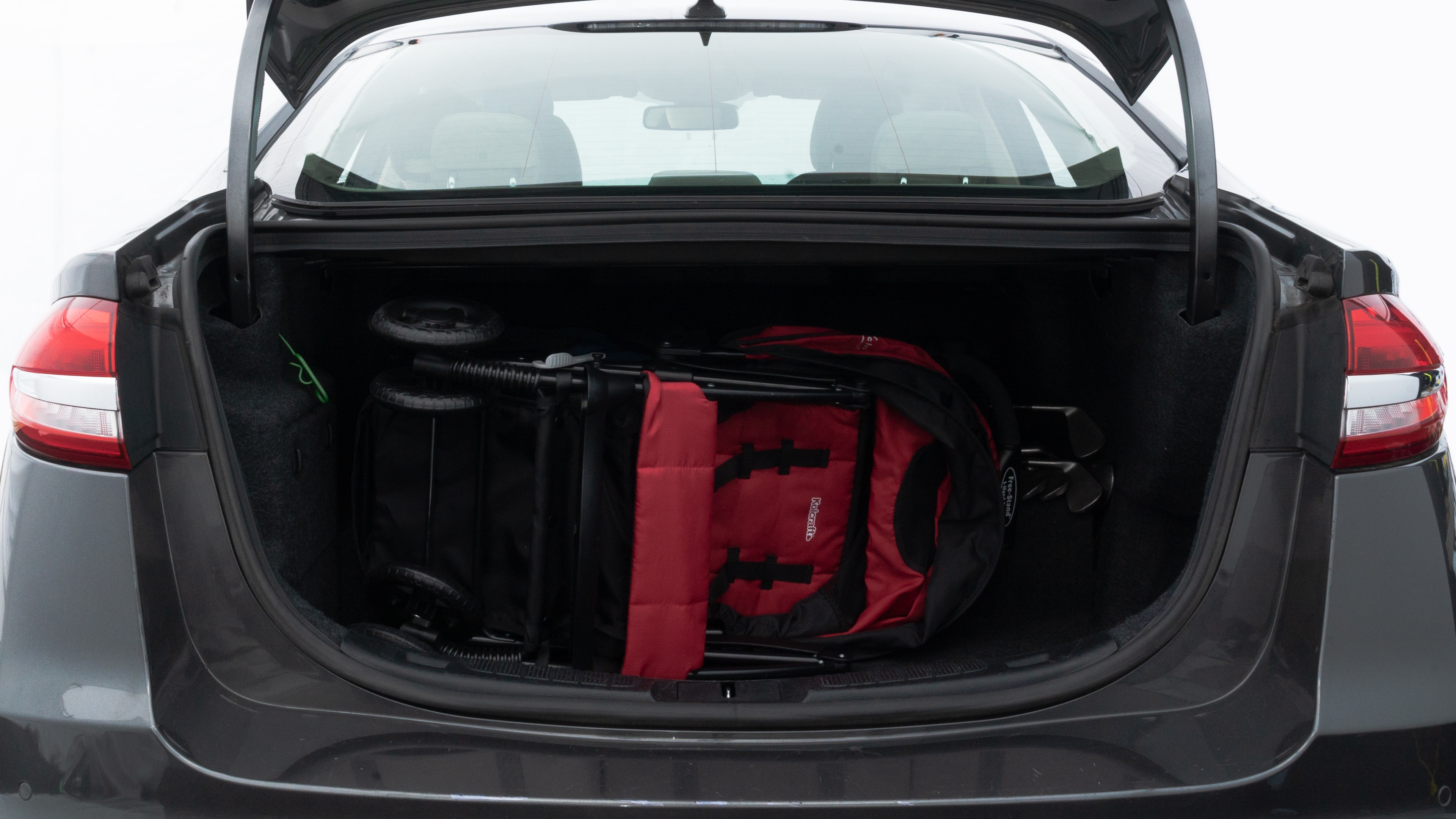 The trunk lid is open showing full view of the trunk. A baby stroller, three grocery carriers, two camping chairs in the carrying bag, and a set of golf clubs are placed inside.